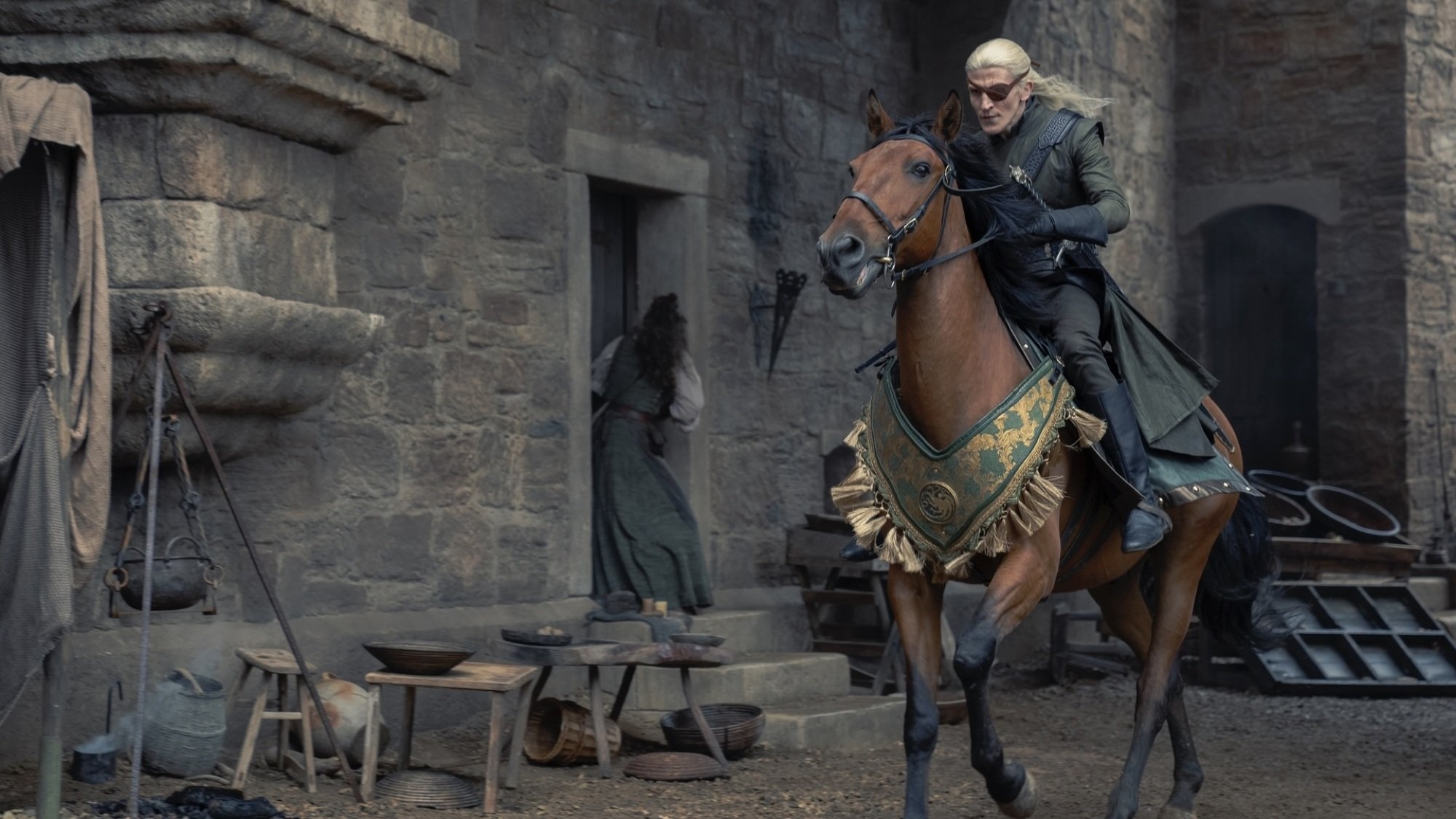 Aemond Targaryen rides a brown horse through King's Landing.