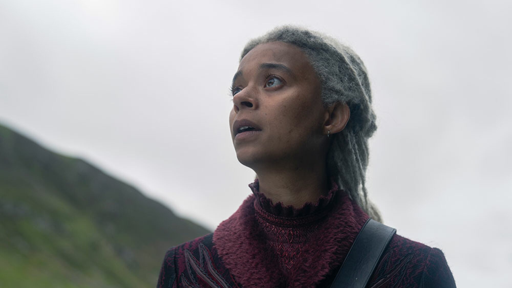 A woman in medieval clothing looks up at the sky, looking shocked.