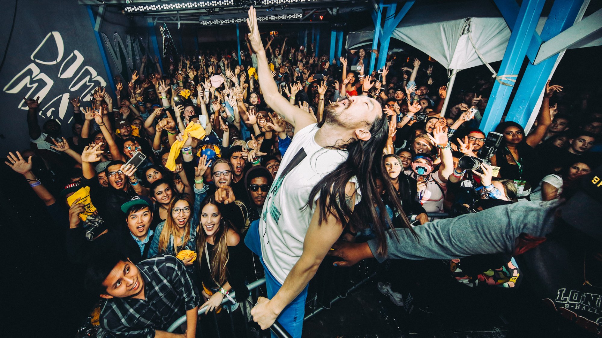 Steve Aoki plays in front of a crowd, everyone with their hands lifted.