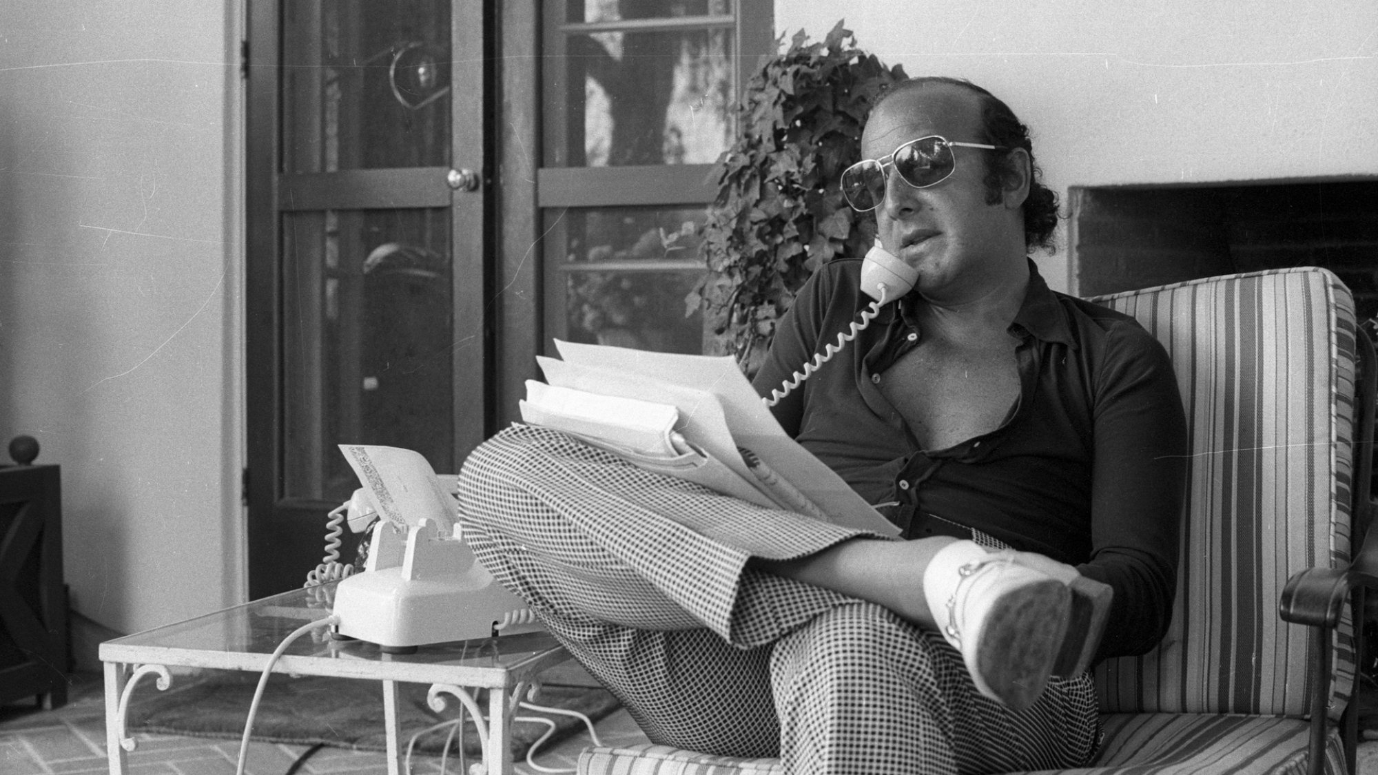 A black and white photo of Clive Davis on the phone shuffling through papers on his porch.