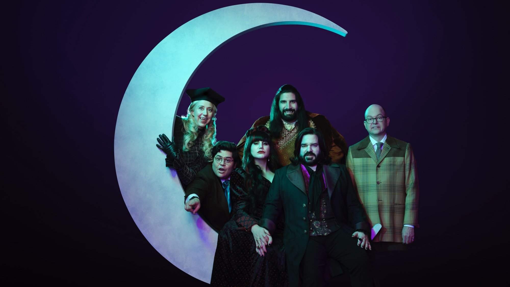 The cast of "What We Do in the Shadows" sitting on a prop crescent moon.