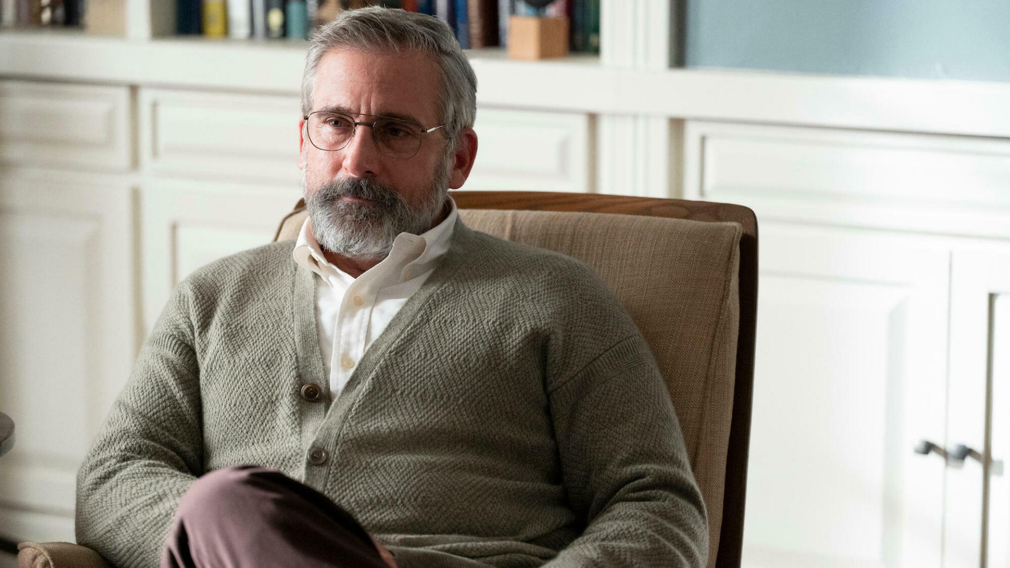 A therapist wearing a beige cardigan sits on a chair in his office. 