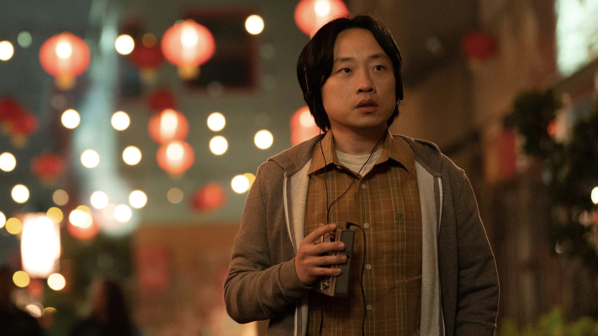 Jimmy O. Yang as Willis Wu walks down a street lit by red Chinese lanterns, listening to a cassette tape.