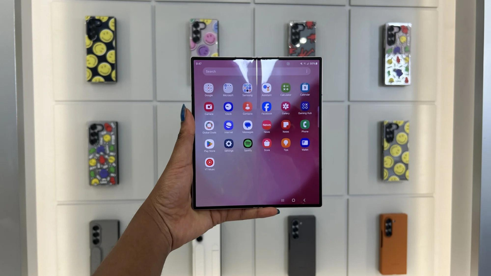 hand holding up Samsung Galaxy Z Fold 6 phone against wall of phone cases