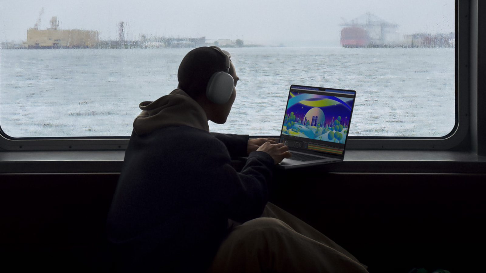 a man working on an apple macbook pro in front of a window looking over a harbor