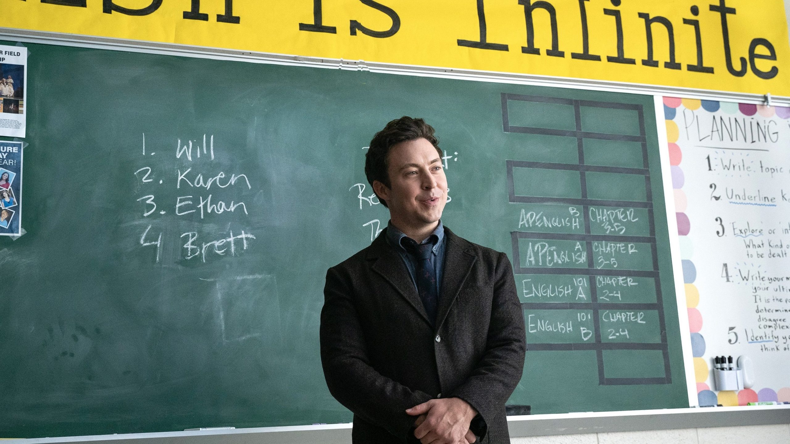 English teacher Evan Marquez stands in front of a blackboard.