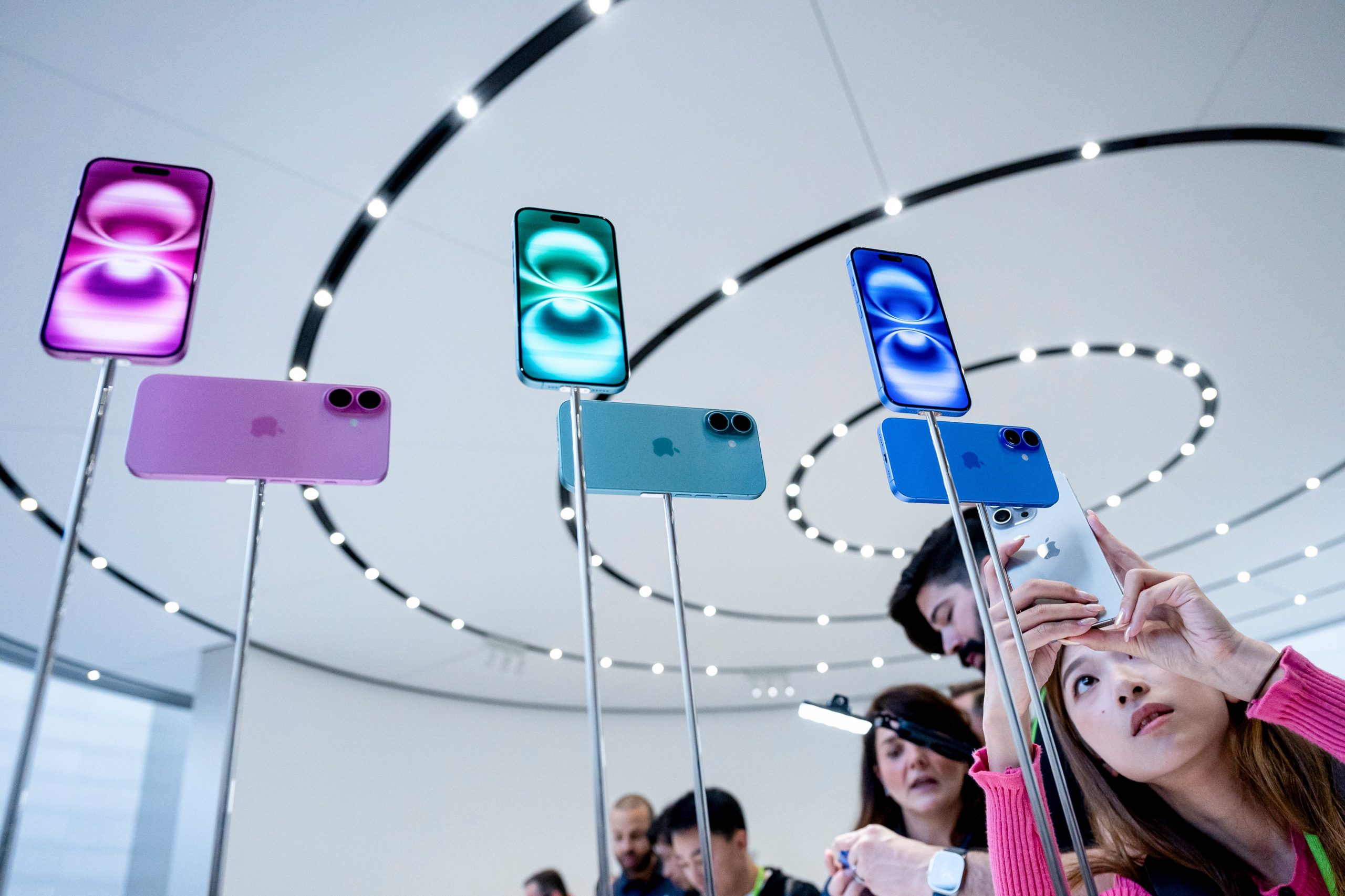 A woman takes a photo of iPhone 16 display models