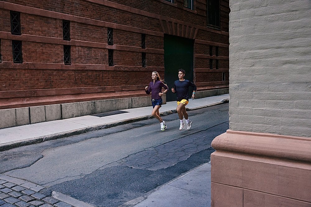 two people running in an industrial setting with brick buildings while they both wear garmin watches