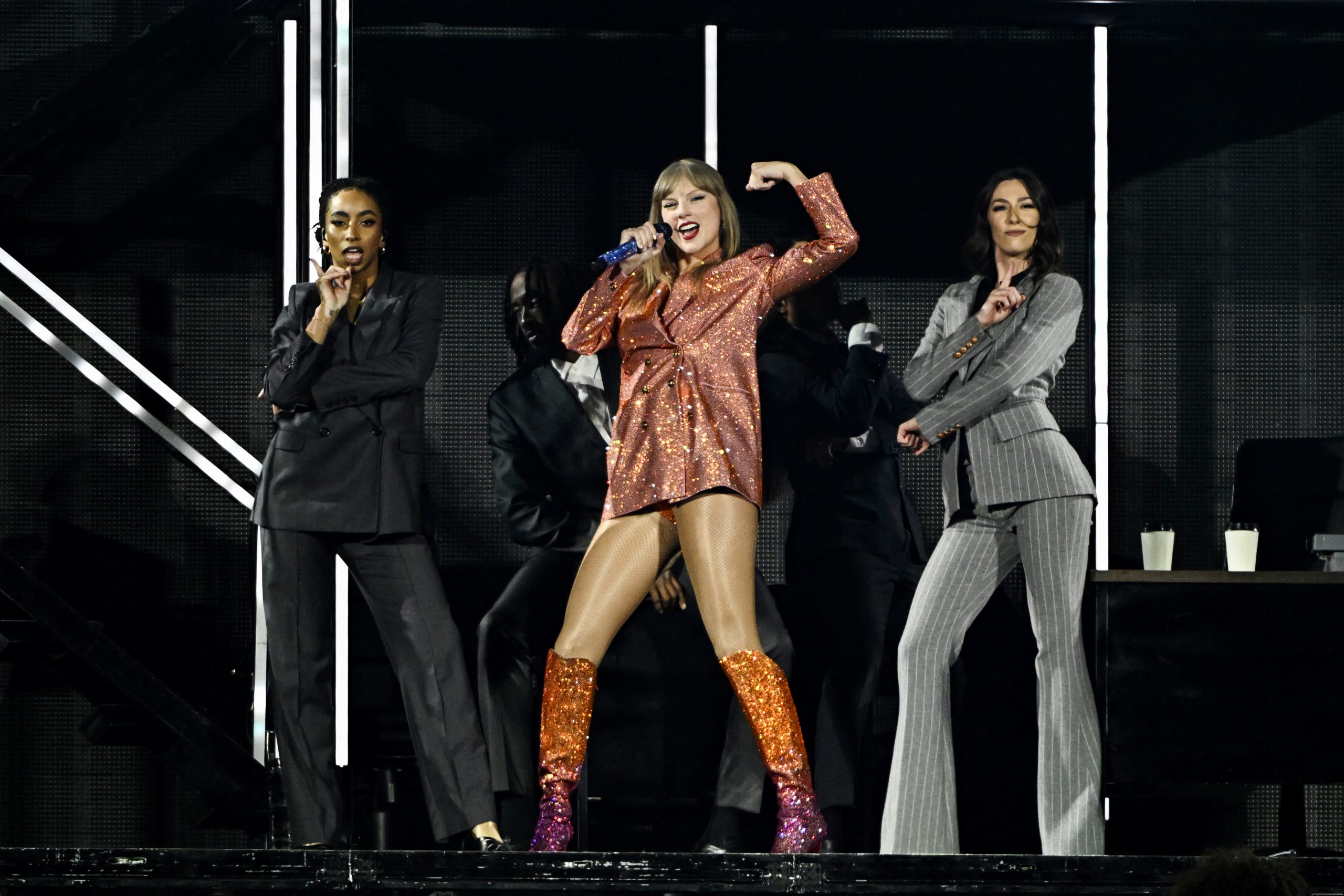 Taylor Swift performing in a blazer with one arm flexed as a demonstration of strength.