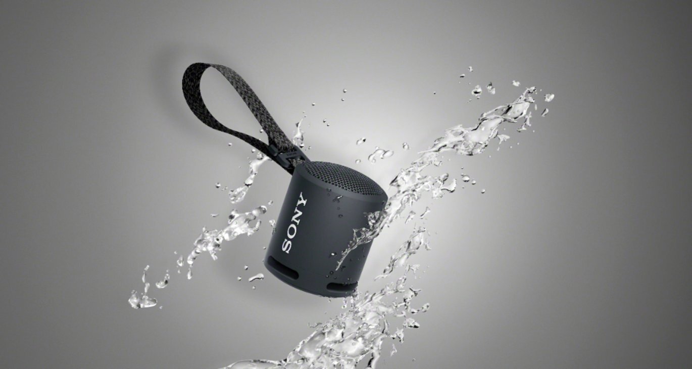 a black portable sony speaker on a gray background with several splashes of water around the small speaker