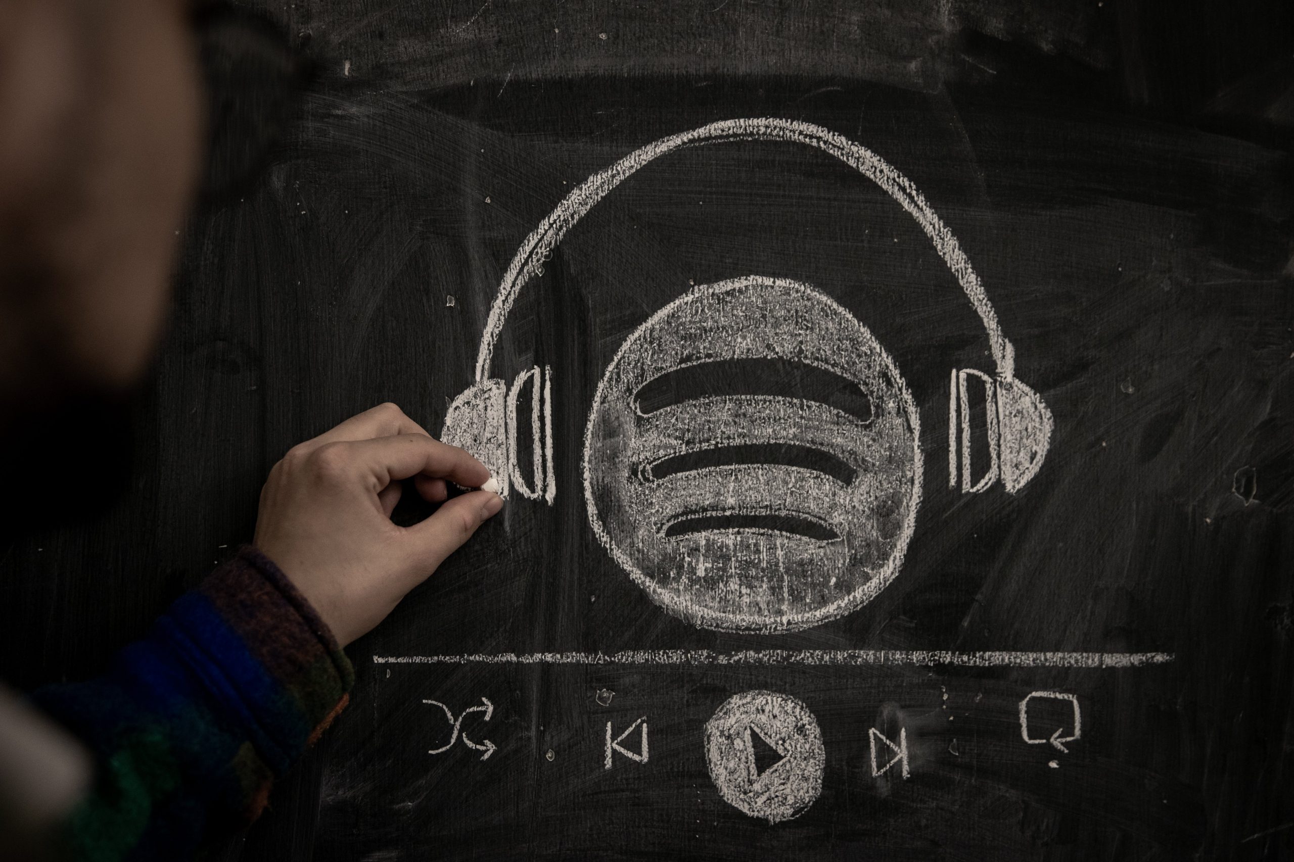 A person drawsingthe Spotify logo wearing a pair headphones in chalk. 