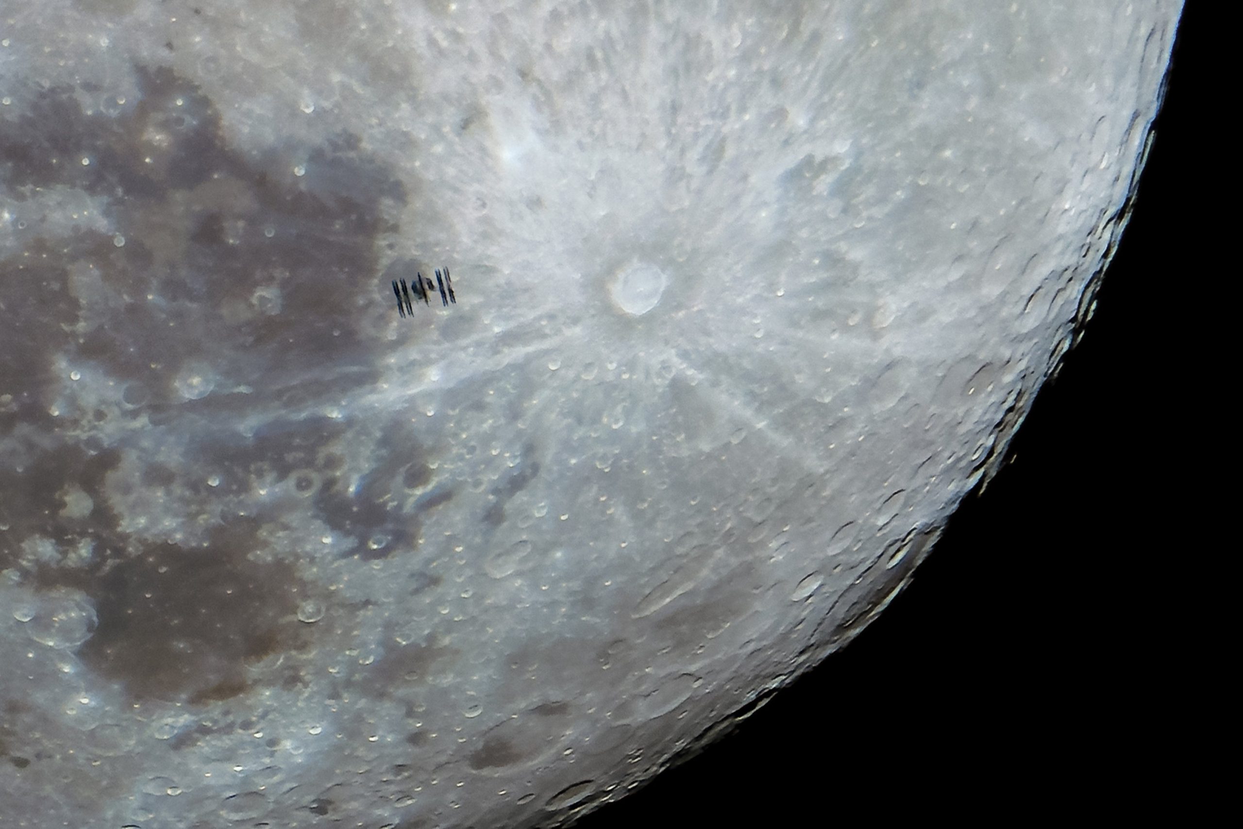 The International Space Station flies in front of the surface of the moon. 