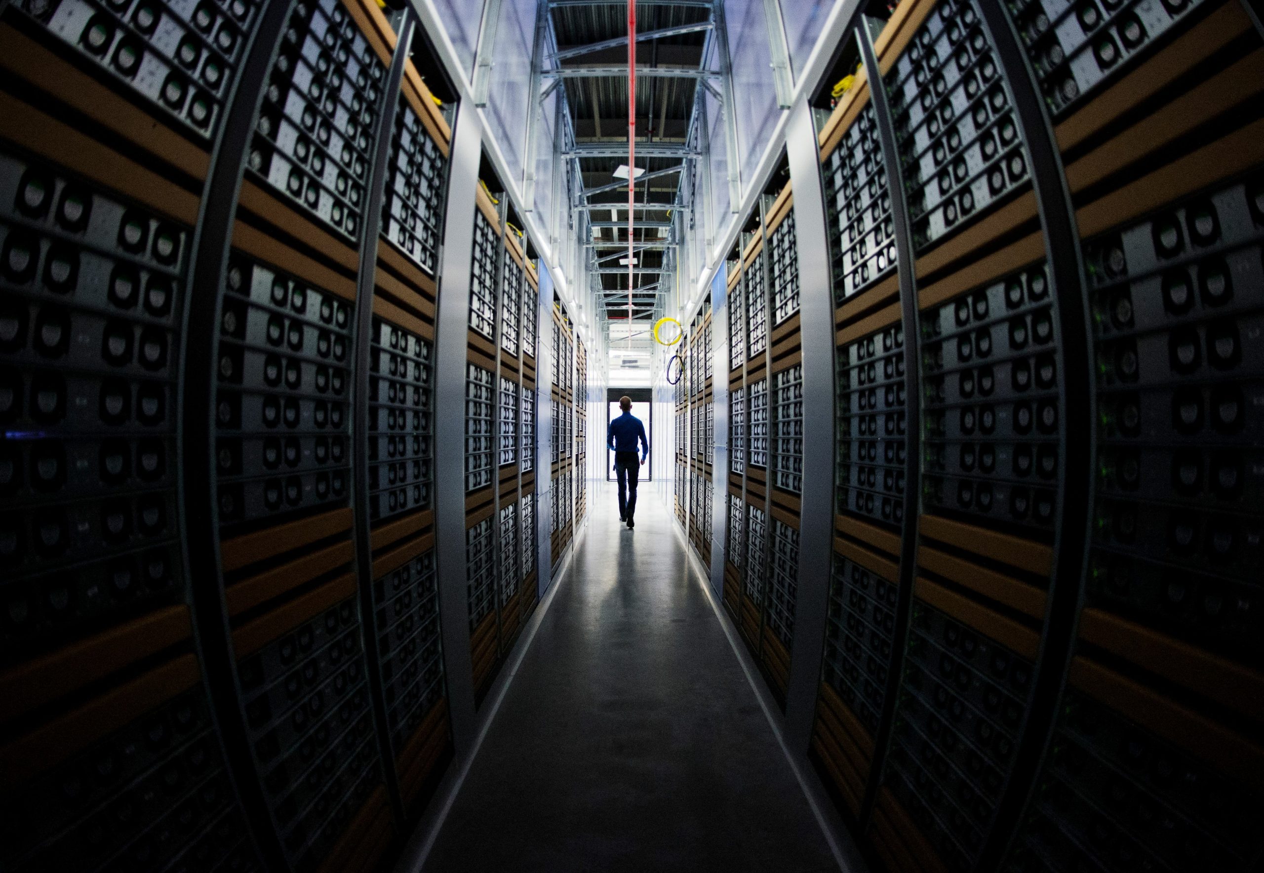 A man in silhouette, walking through racks of computers in a data center.