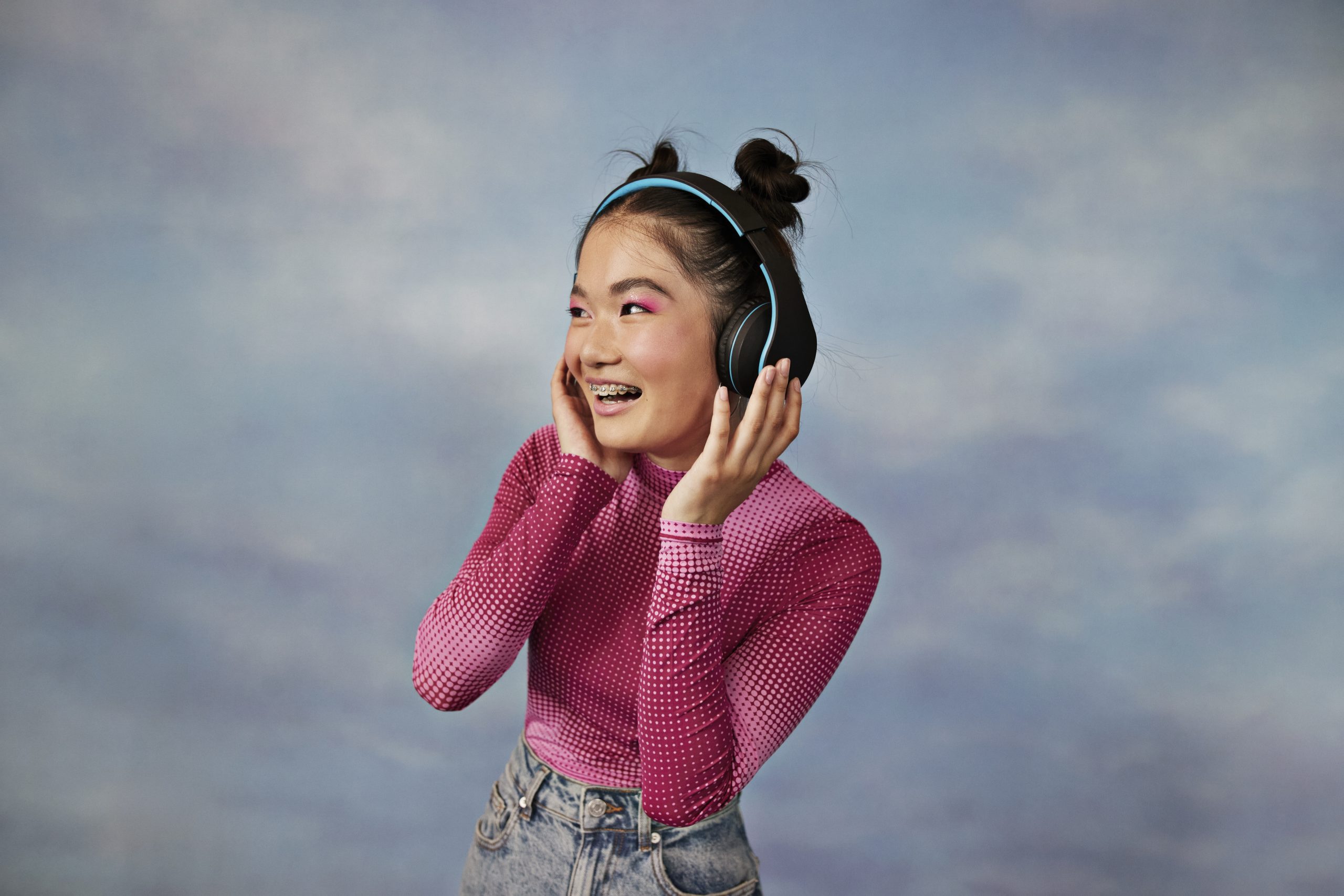 Cheerful teenage girl listening to music through wireless headphones against colored background