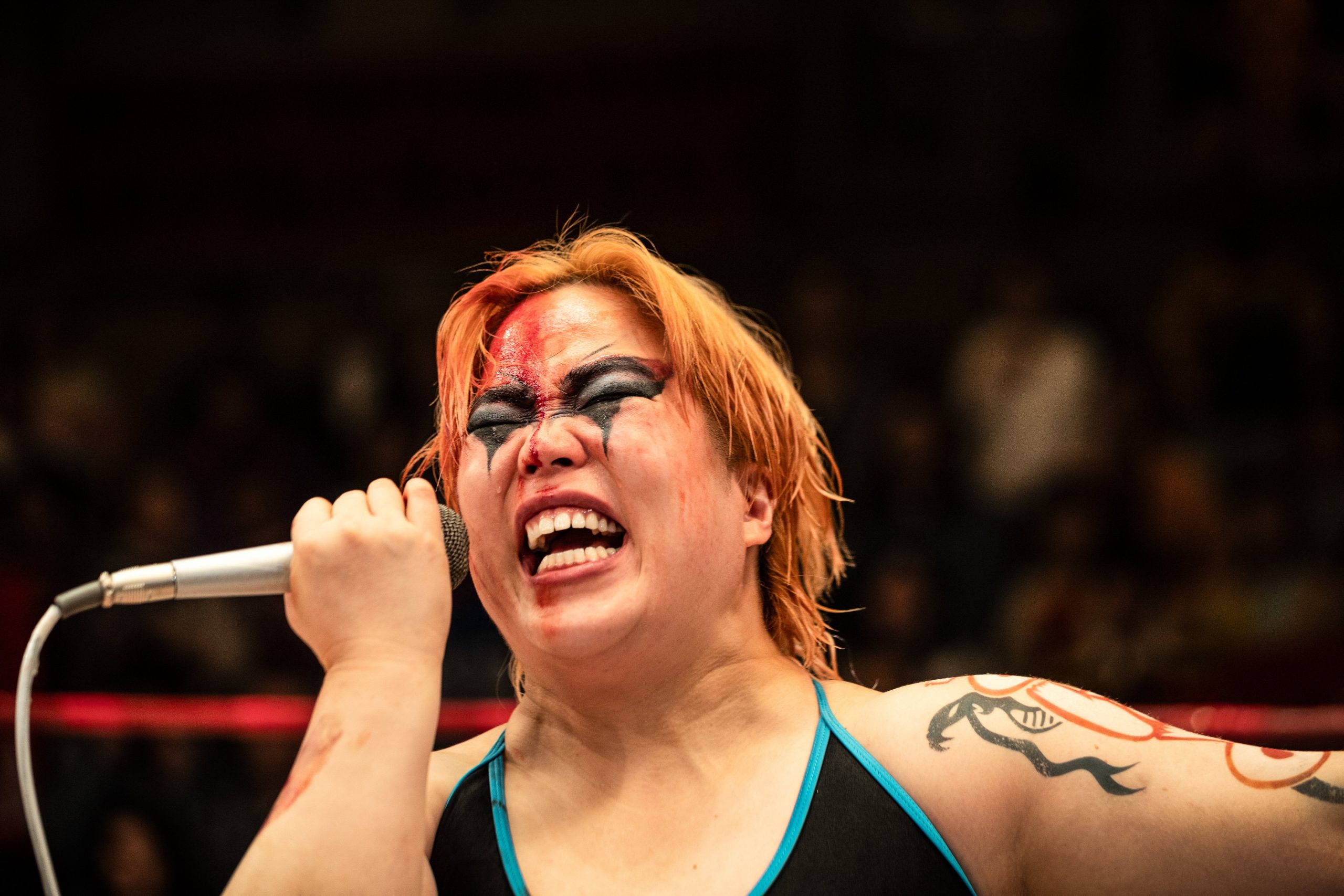 Professional wrestler with dramatic face paint and a microphone, passionately speaking during a match.