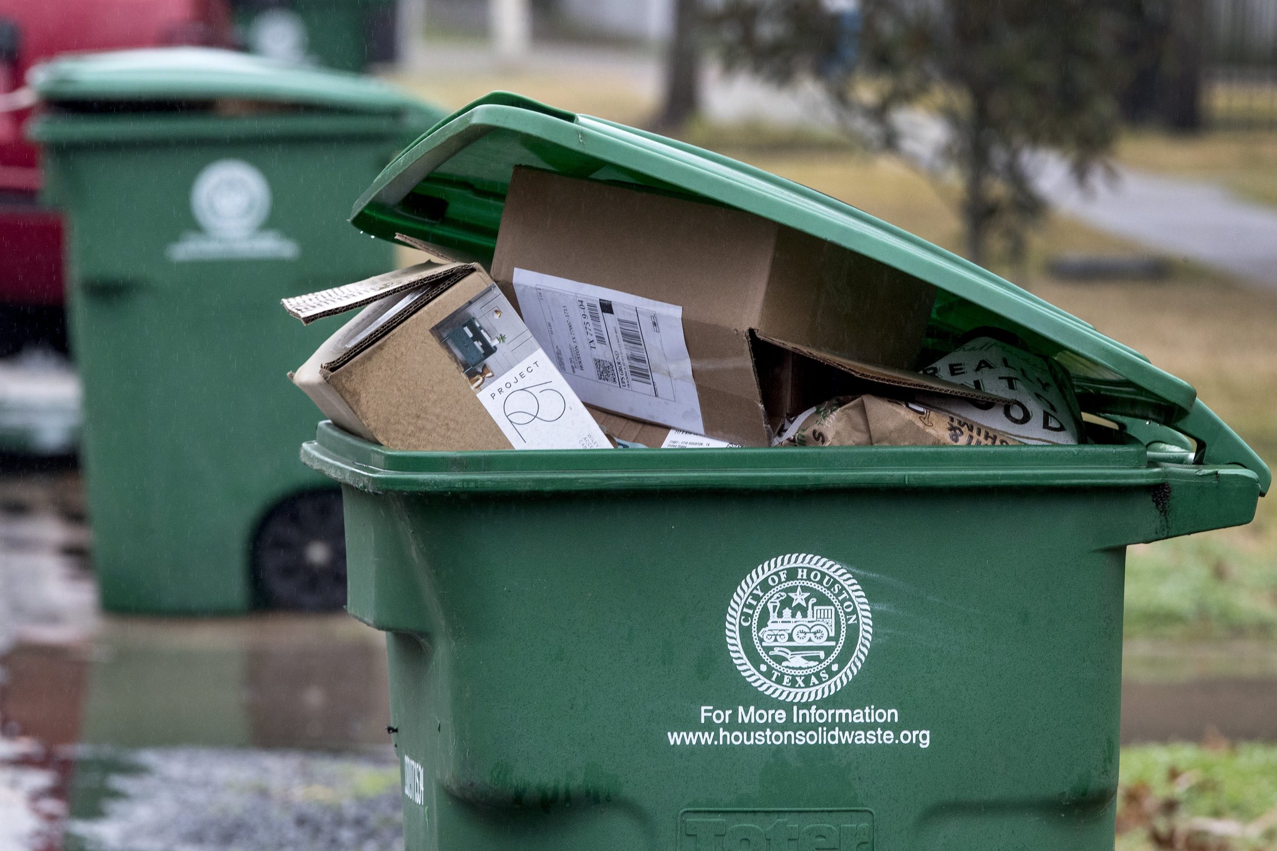 A green recycling bin with the city of Houston logo, full of cardboard boxes. 