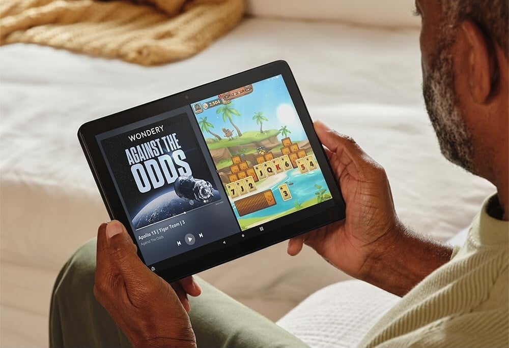 a person holds an Amazon fire HD 10 tablet while sitting on a cream colored couch