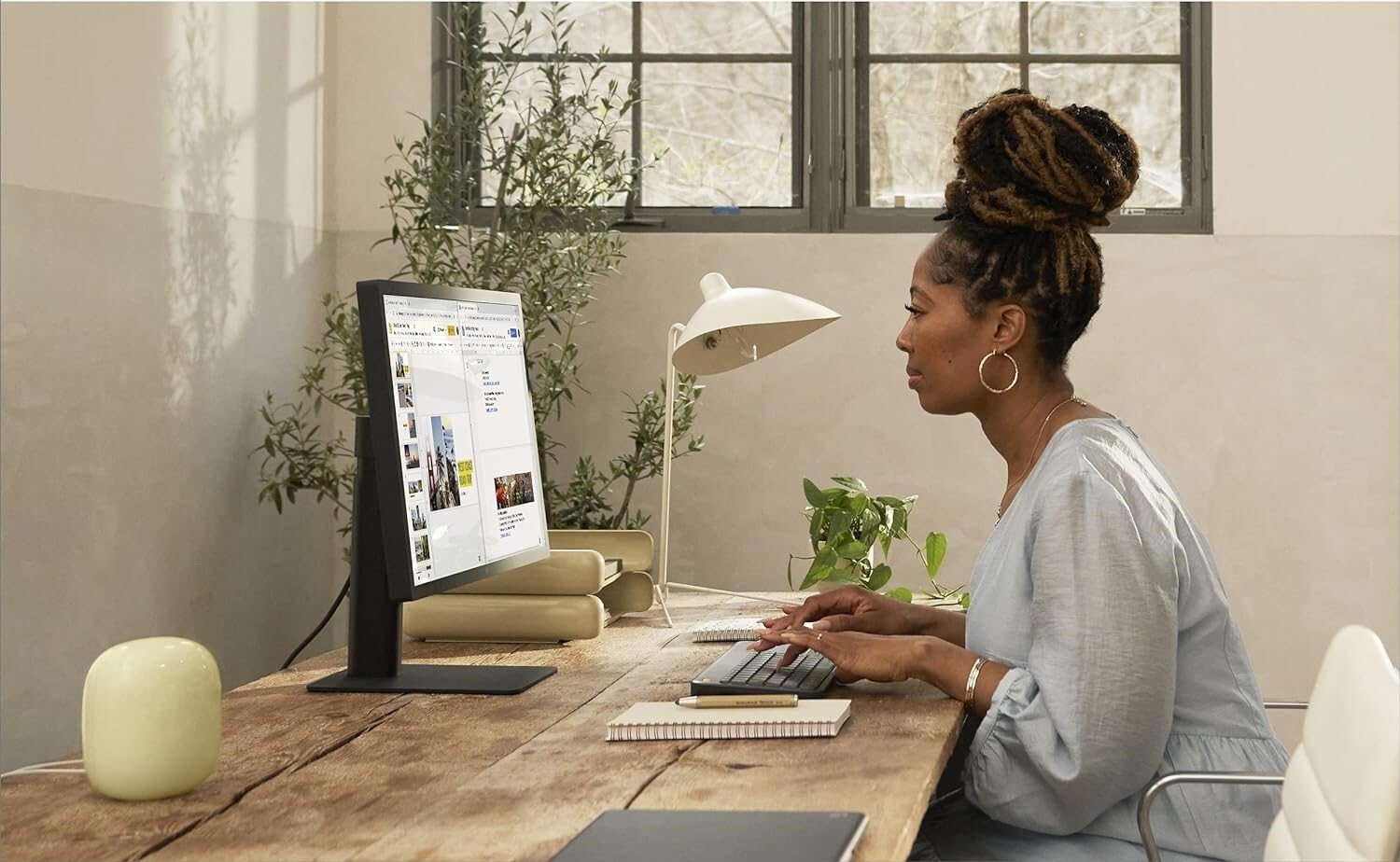 a person sits in front of a desktop monitor while a google nest wifi pro router sits on her desk