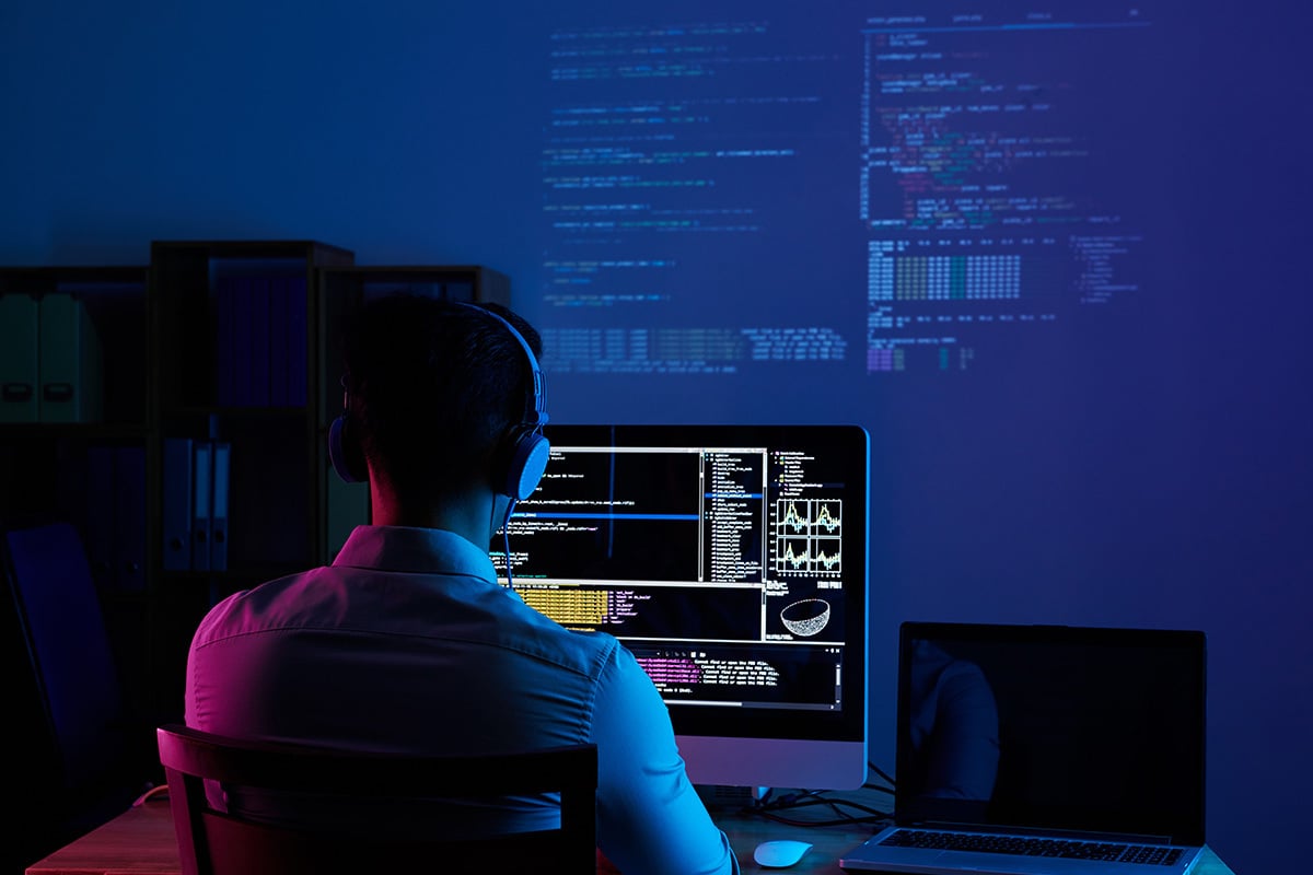 man working with multiple monitor screens in dark room