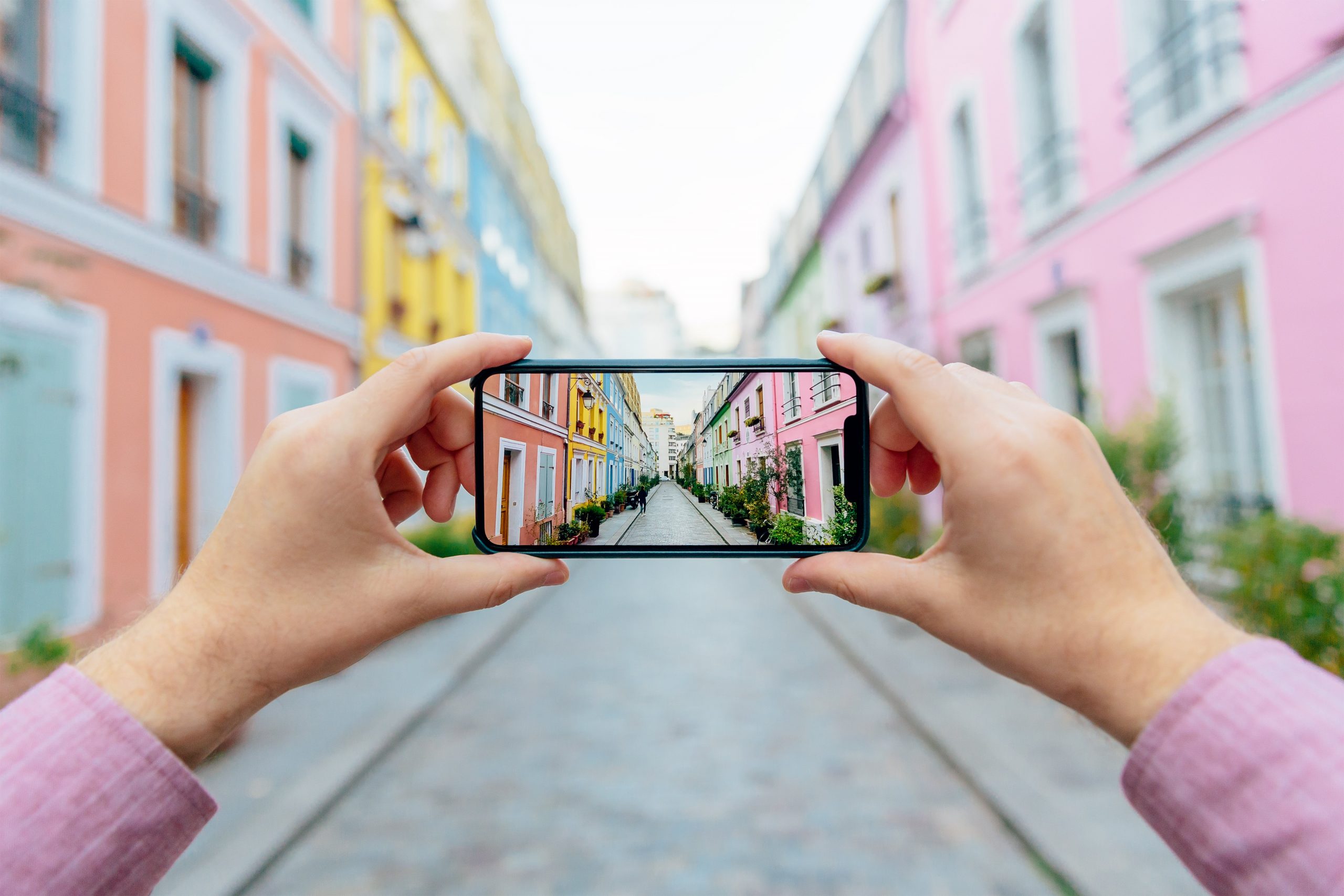 Personal perspective of a man photographing colorful street Rue Cremieux with smartphone.