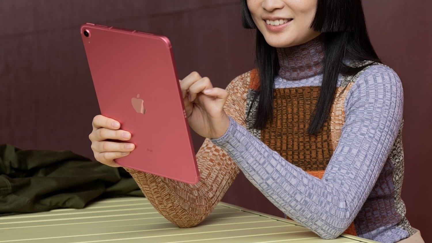 person sitting at table and smiling while using pink 10th generation ipad