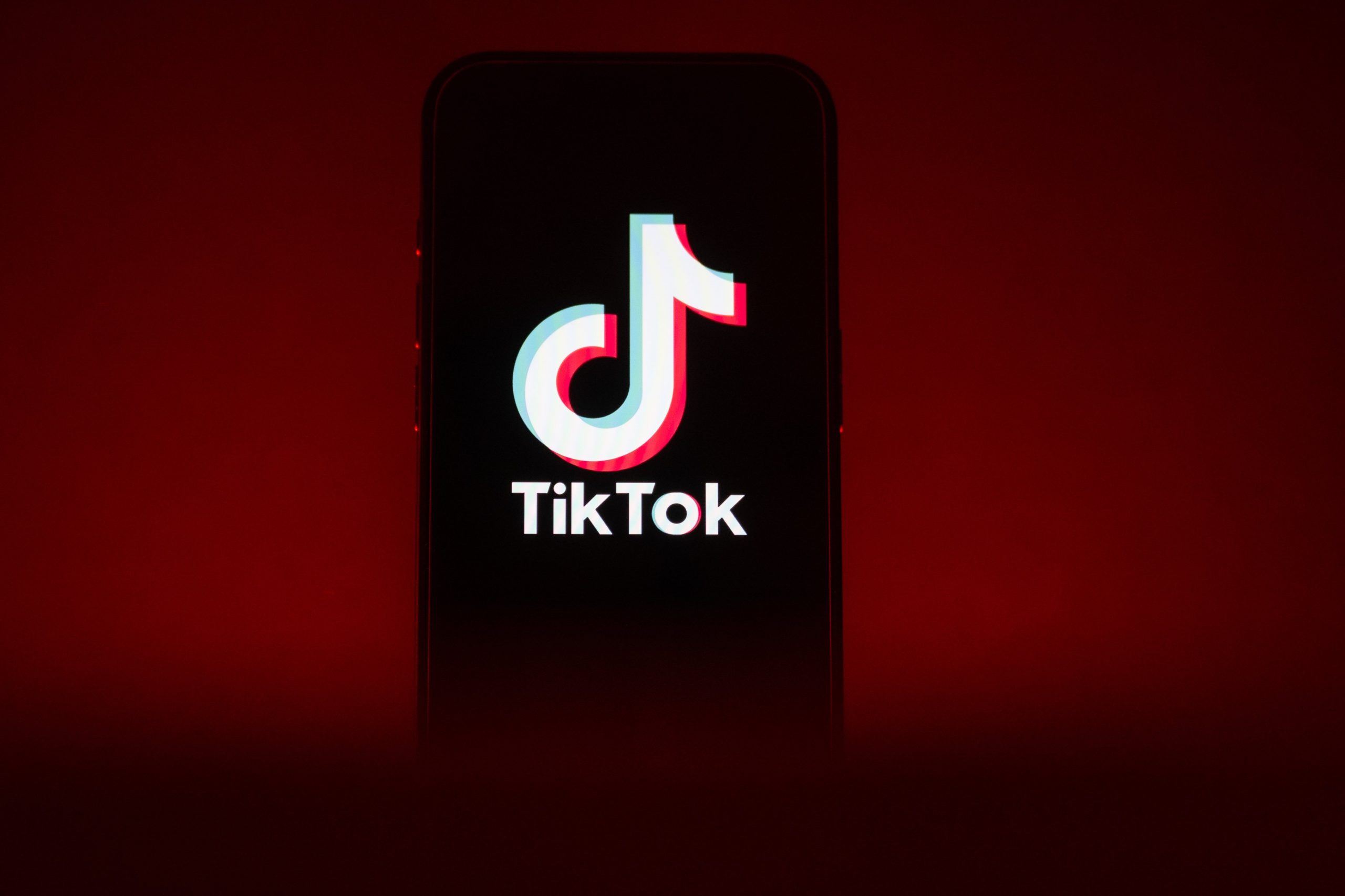 A phone in front of a red background showing the TikTok logo.