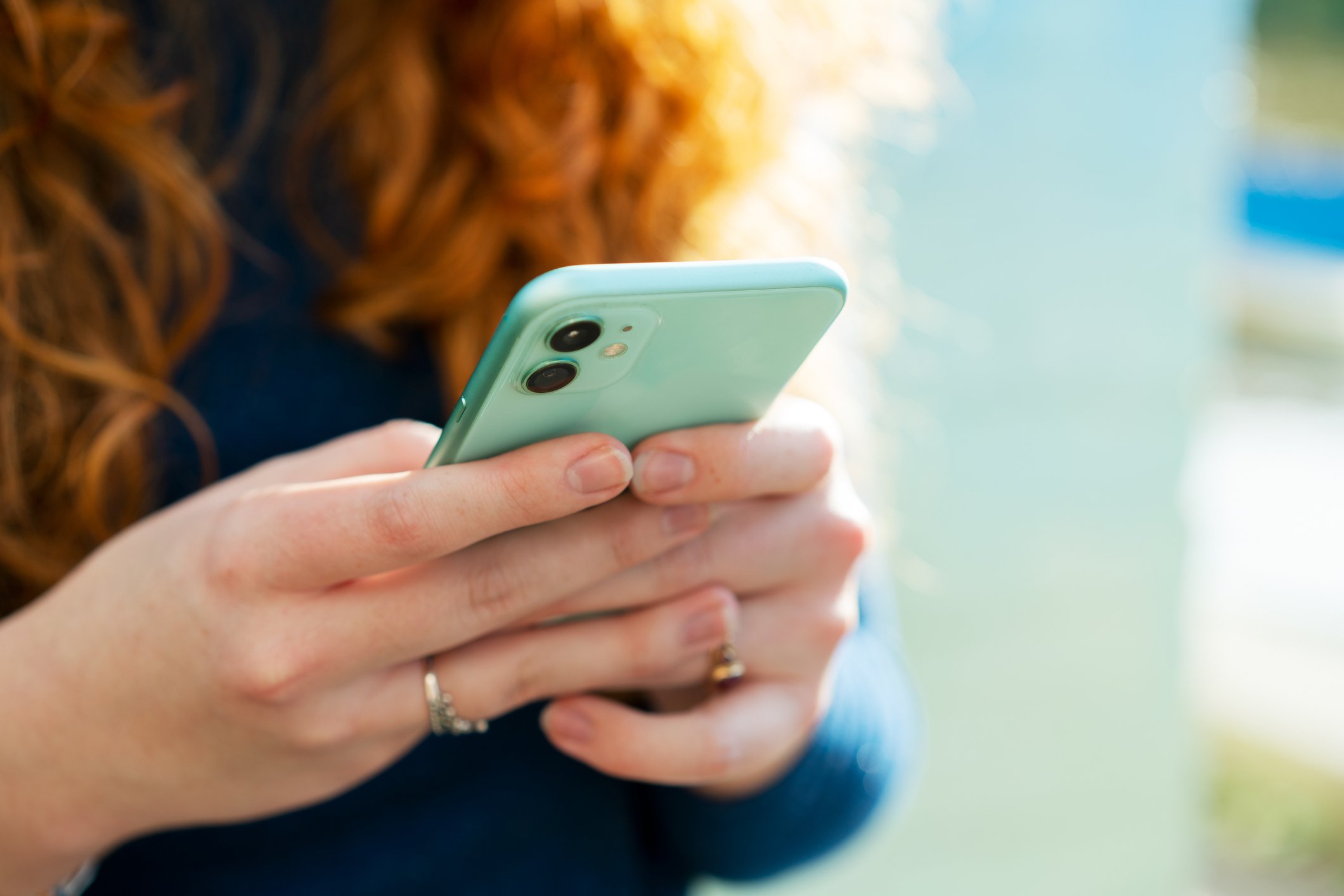 Close up of red-haired woman using smart phone with turquoise cover. 