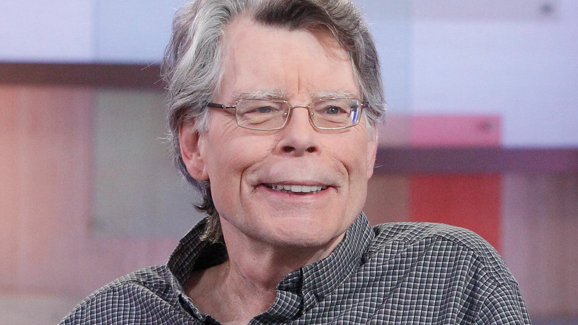 Stephen King wearing a shirt and grinning while looking at someone off-camera.