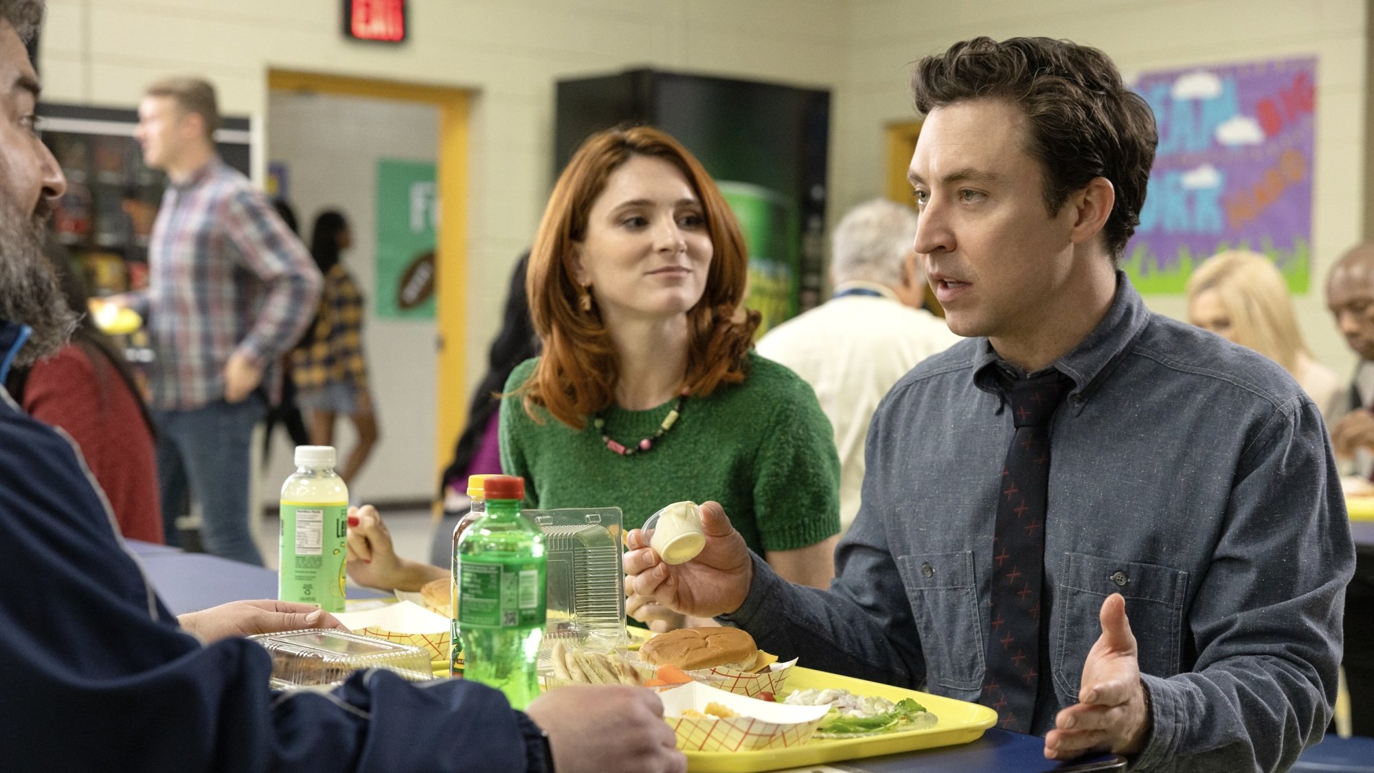 Teachers Markie, Gwen, and Evan eat lunch in a high school cafeteria.