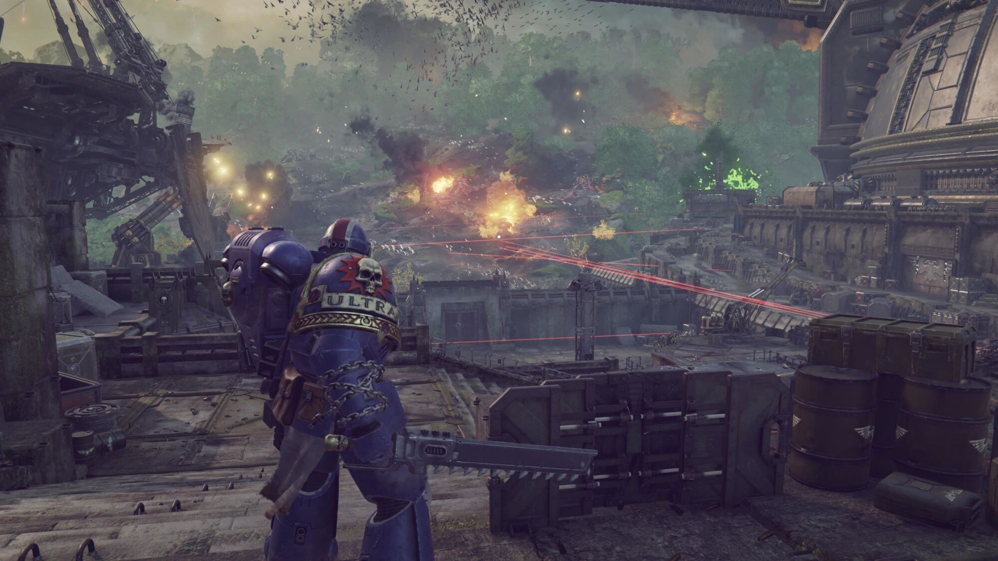 The Space Marine overlooks a chaotic battlefield with explosions and gunfire, possibly planning an assault. The environment is heavily industrial, and the HUD suggests this is part of a mission