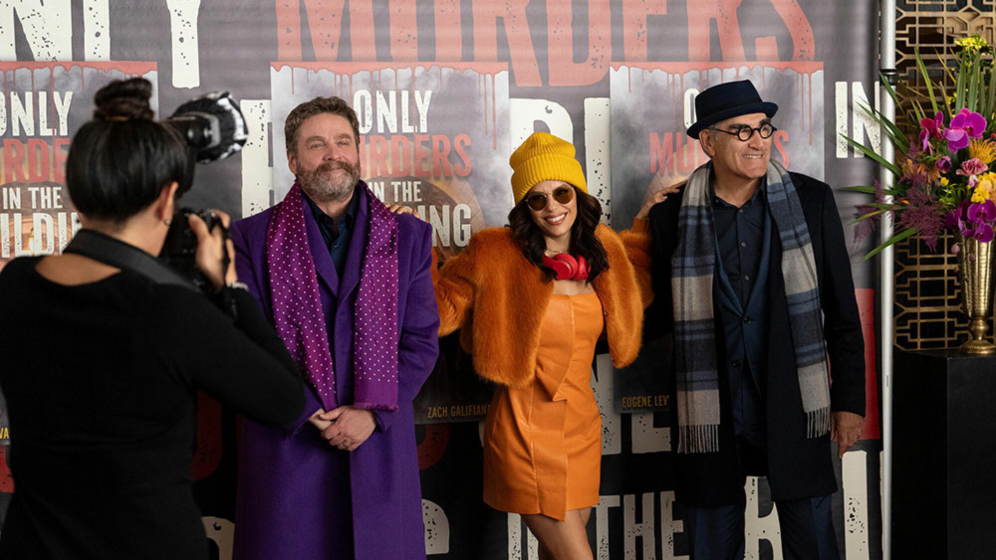 Two men and a woman stand in front of a giant movie poster while a photographer takes photos of them.