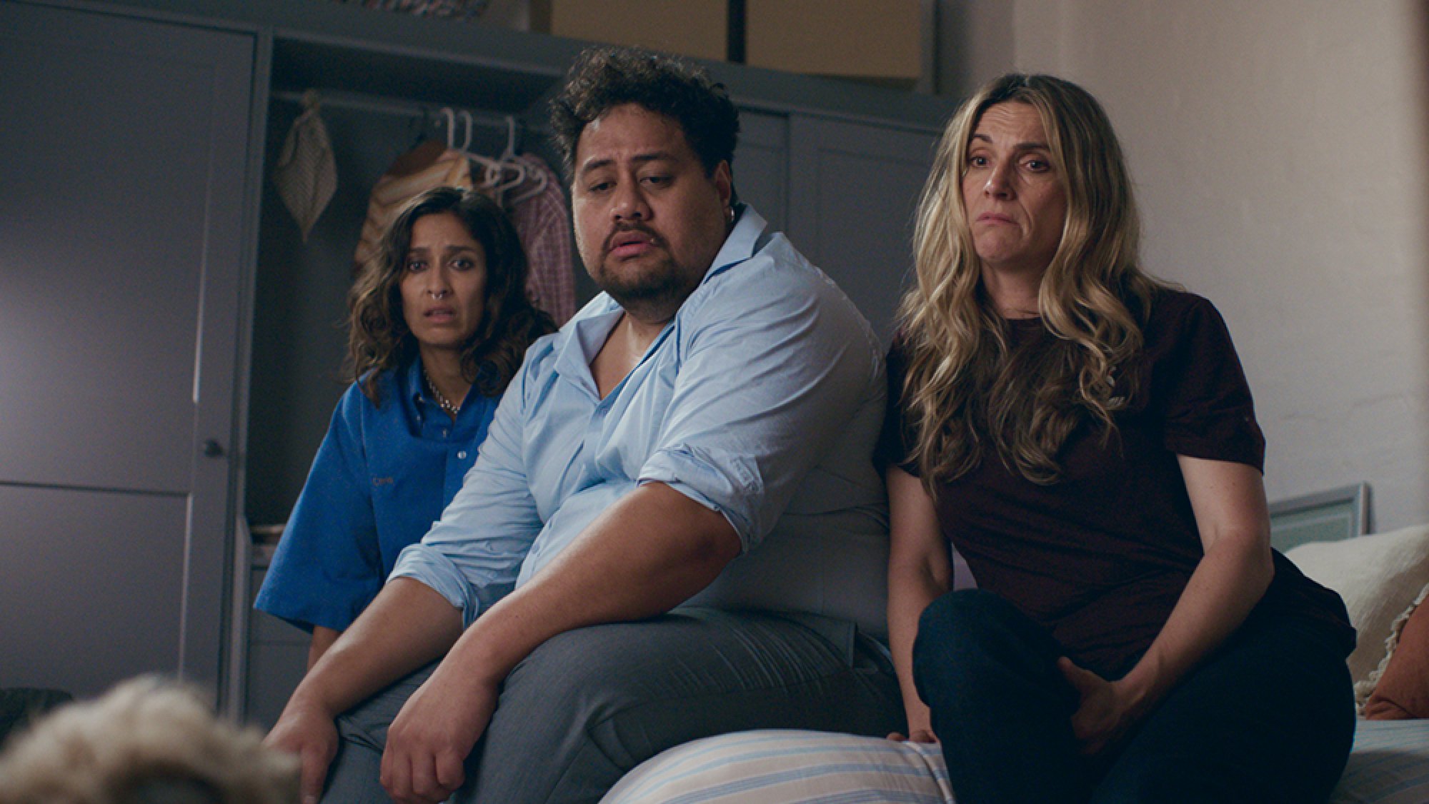 A man and two women sit on a bed staring at a dog that's slightly off-camera.