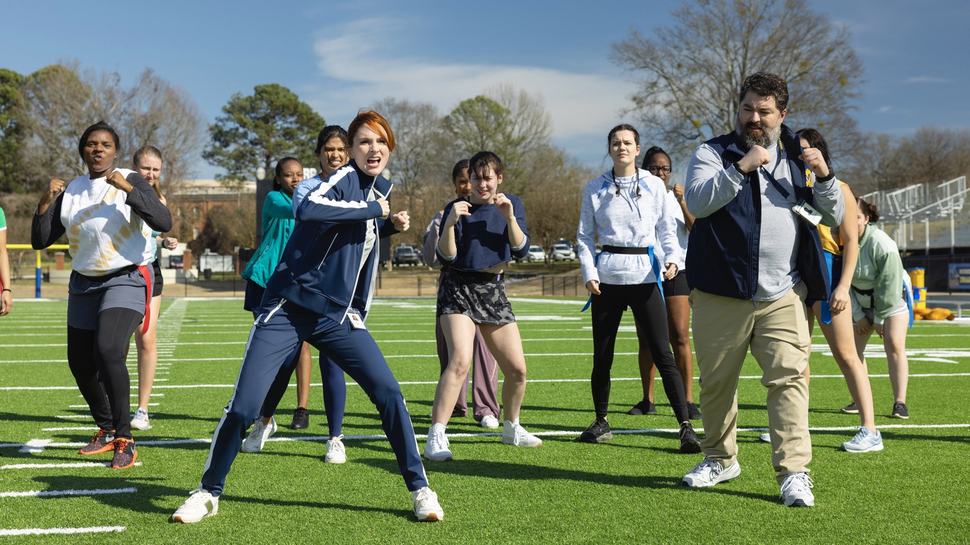 Gwen and Markie teach a group of girls self-defense on a football field.