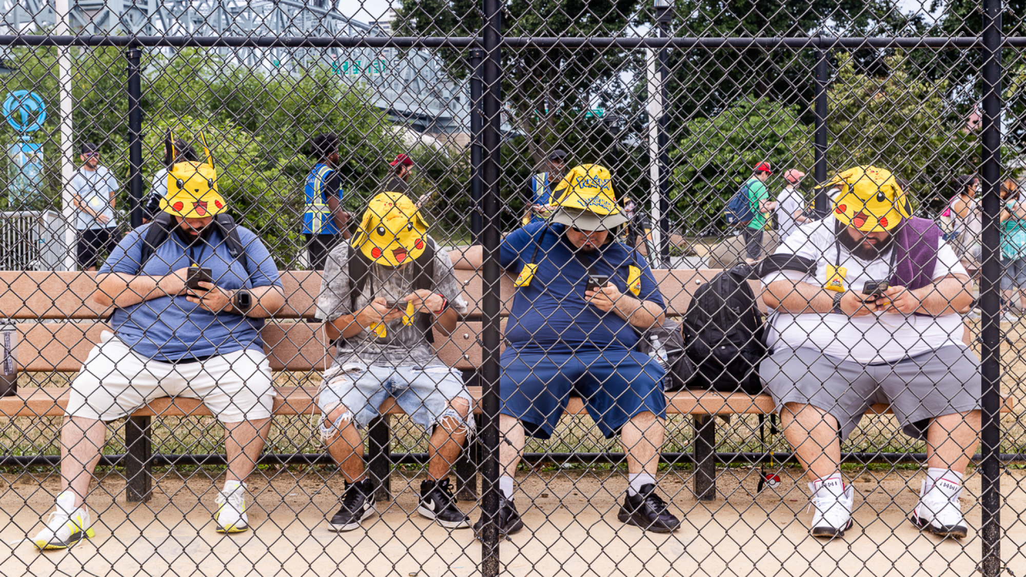 Four people in Pikachu hats sits on a bench playing Pokémon GO.