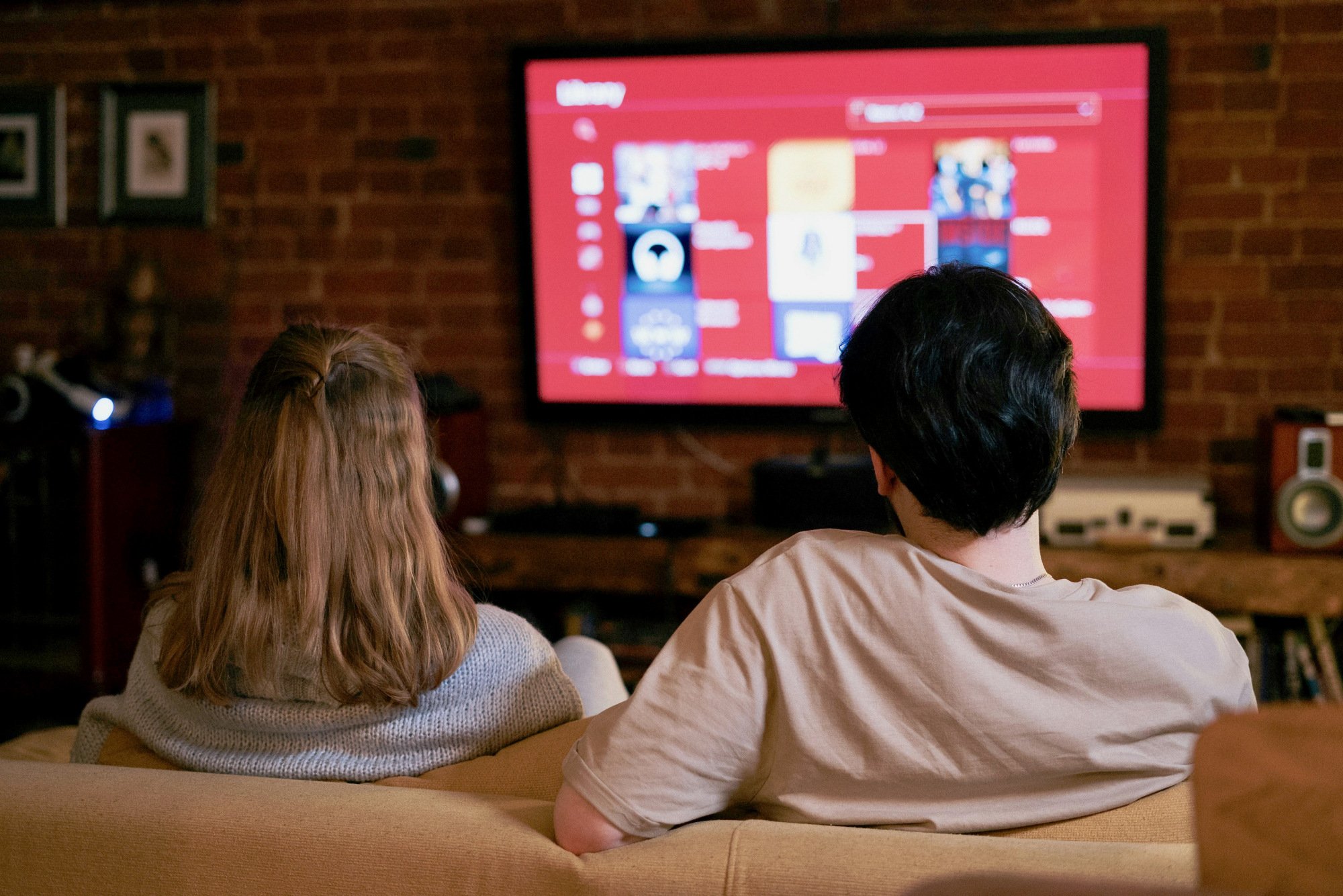 young man and woman watching smart TV on brick wall