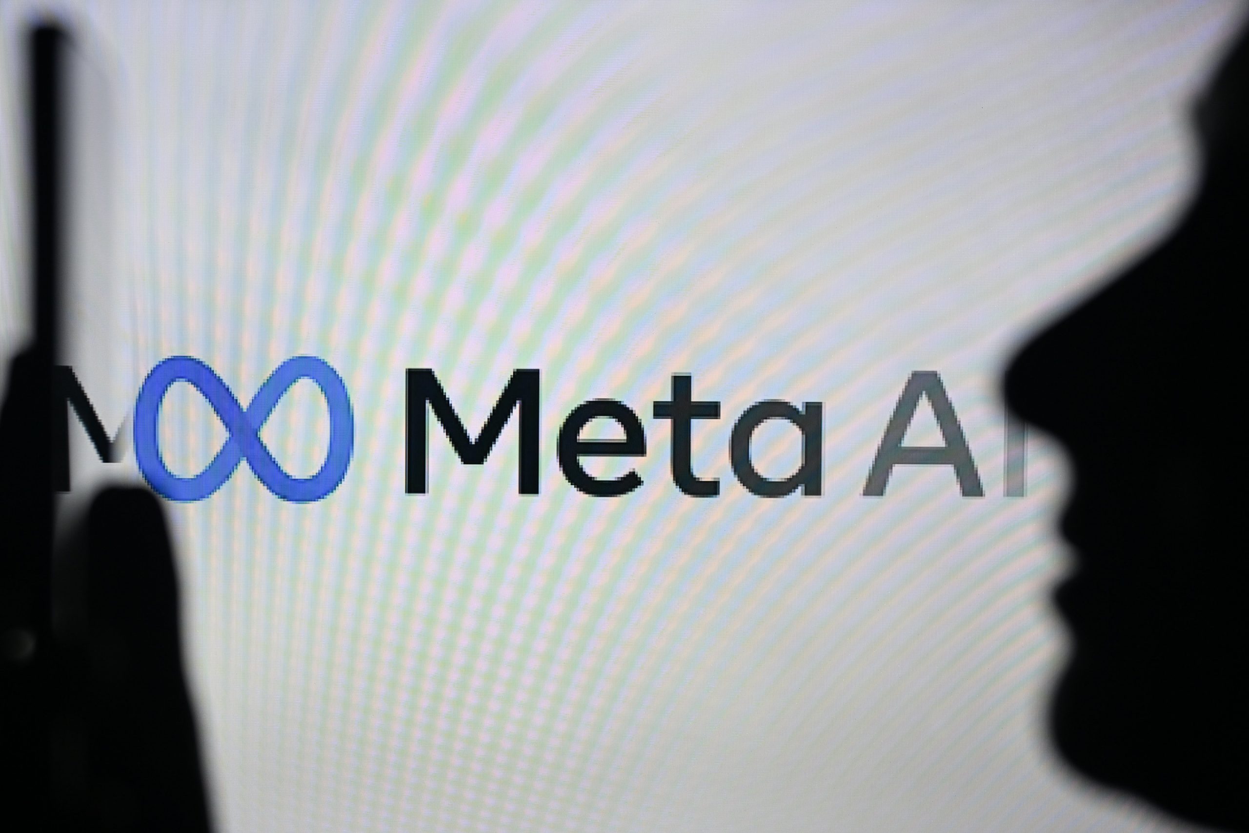 A person holding a cell phone in front of the Meta AI logo displayed on a computer screen, on April 29, 2024, in Edmonton, Canada.