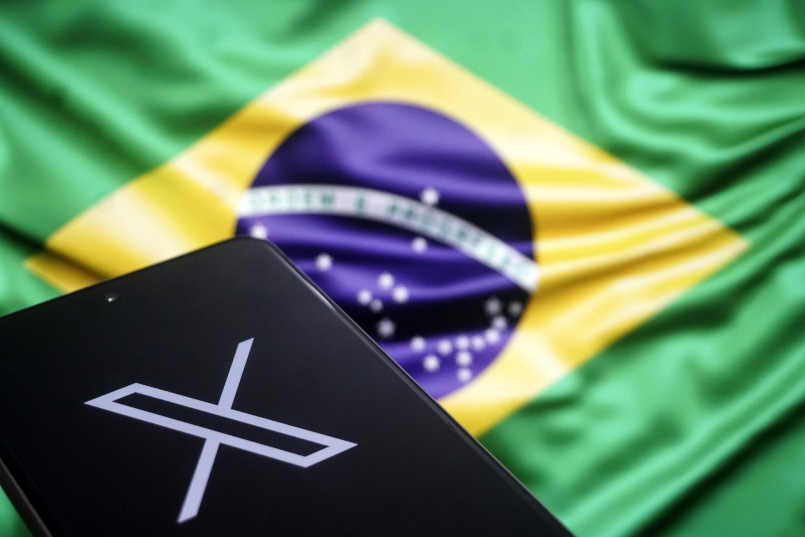 x logo on phone in front of brazilian flag