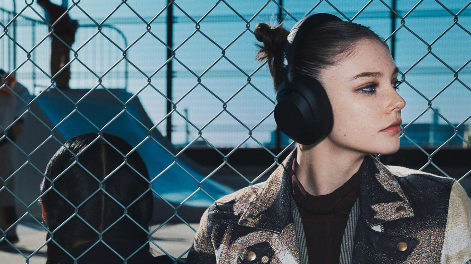 A person standing against a chainlink fence wearing a pair of Sony ULT headphones