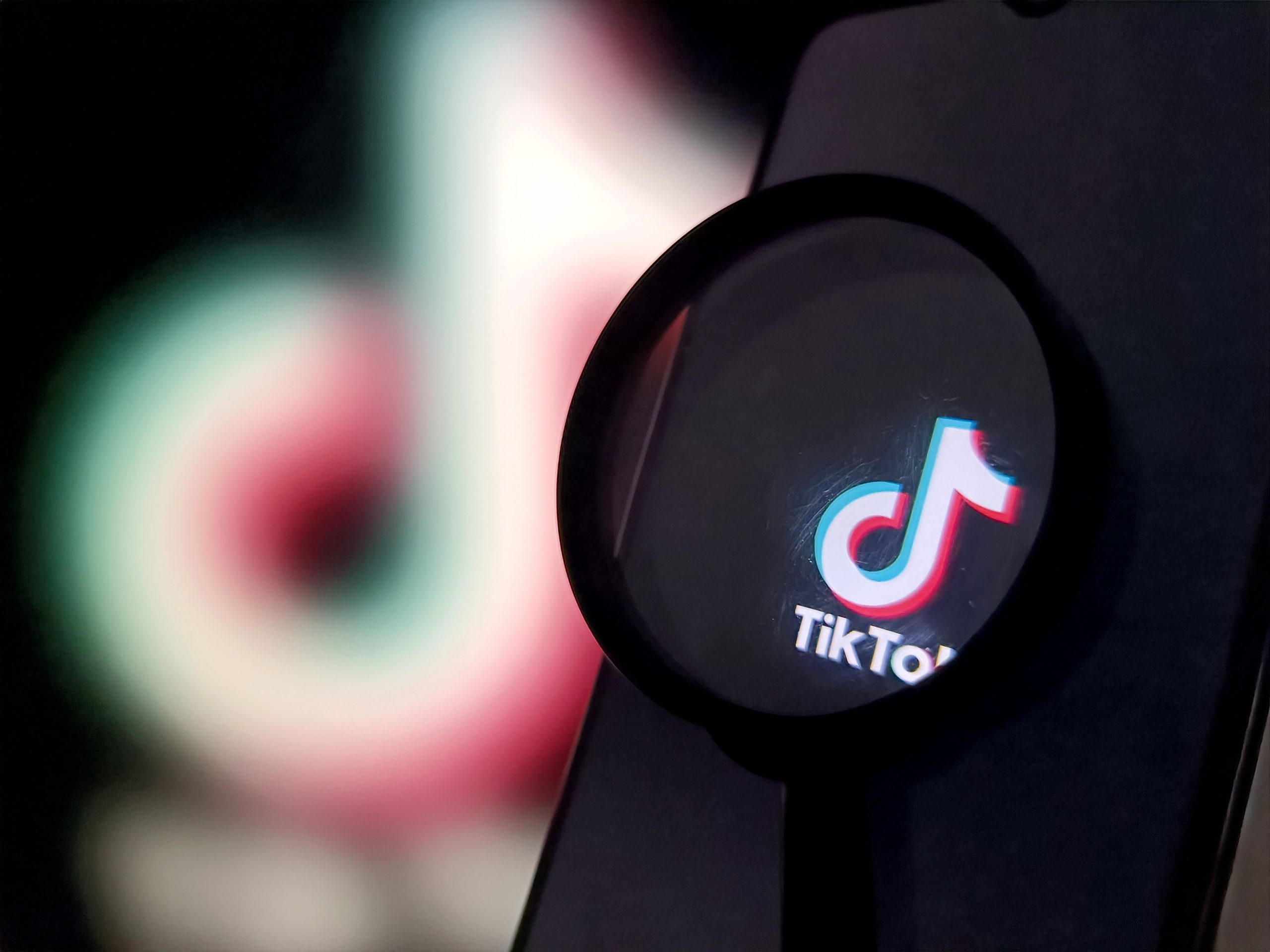 A magnifying glass magnifies a TikTok logo on a phone screen.