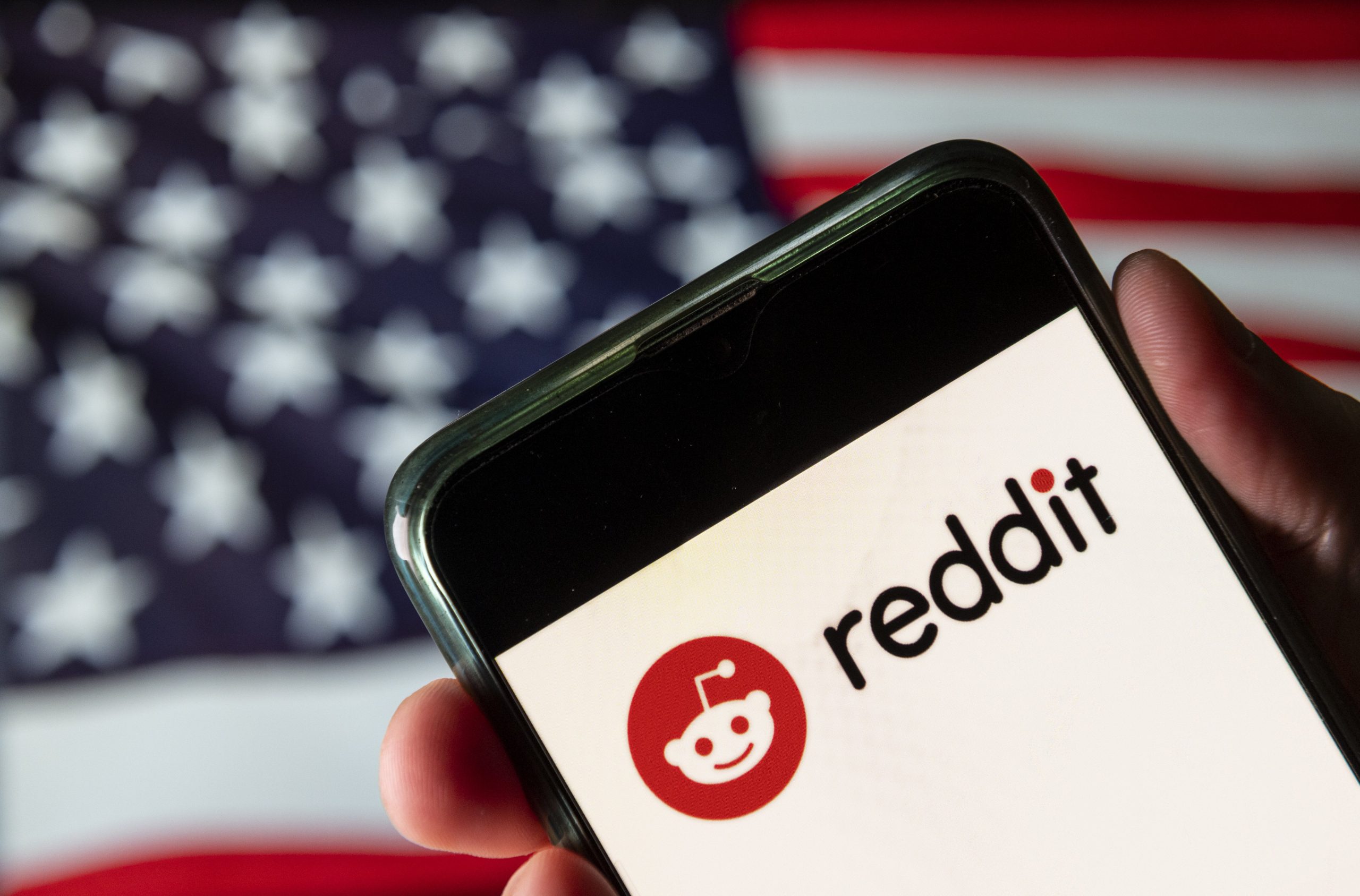 A phone displaying the Reddit logo in front of an American flag.