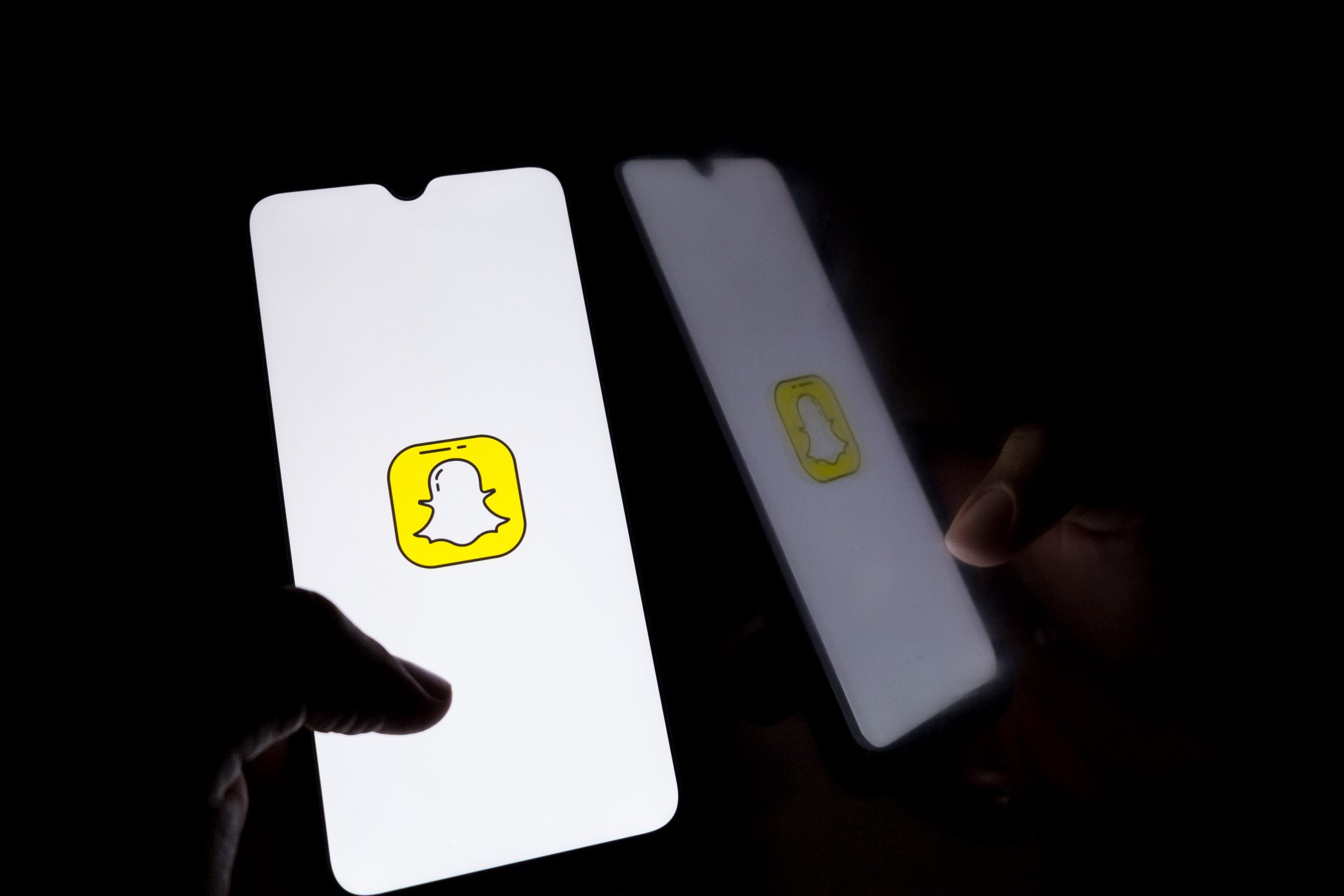 A hand holds a glowing phone showing the Snapchat logo in a dark room.