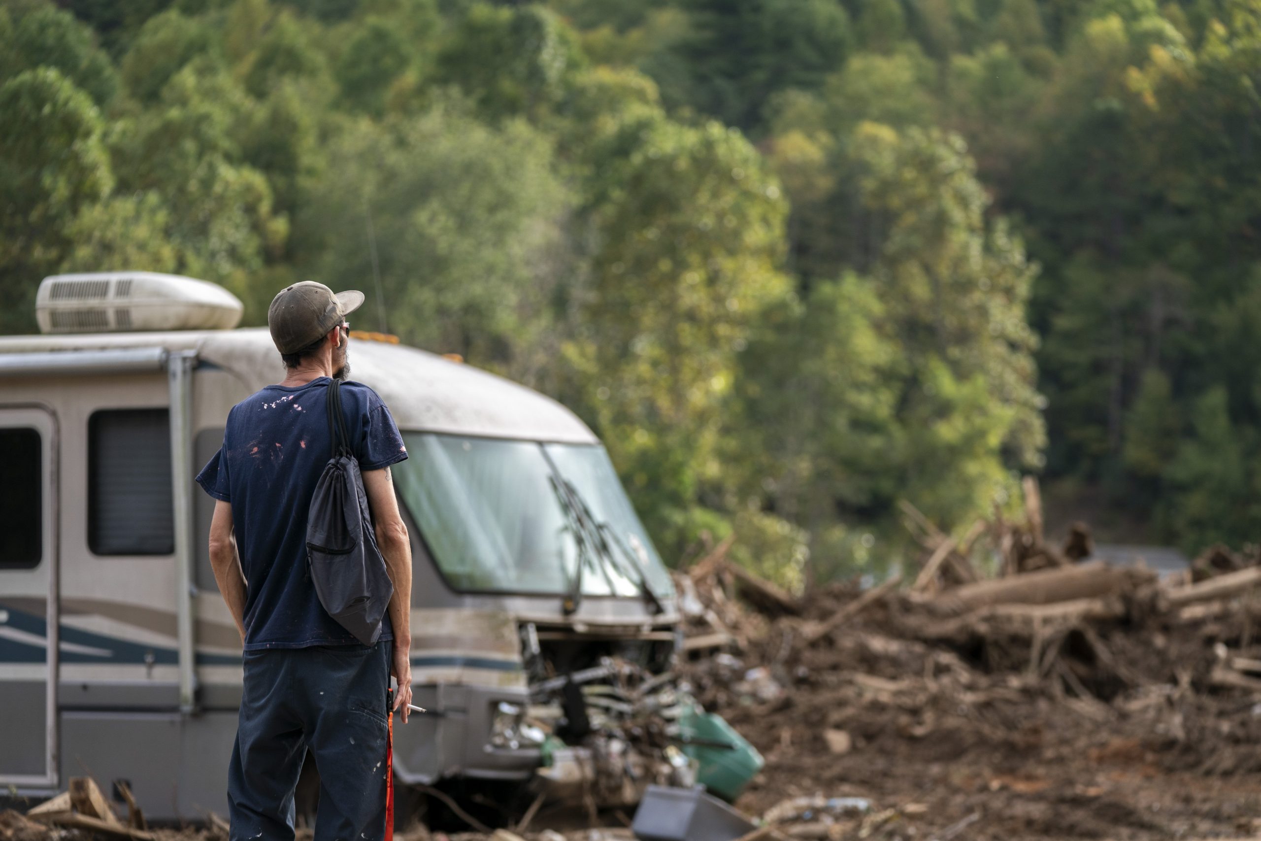 A man stares out at a piece of land full of debris, including the rubble of a home and a destroyed RV.