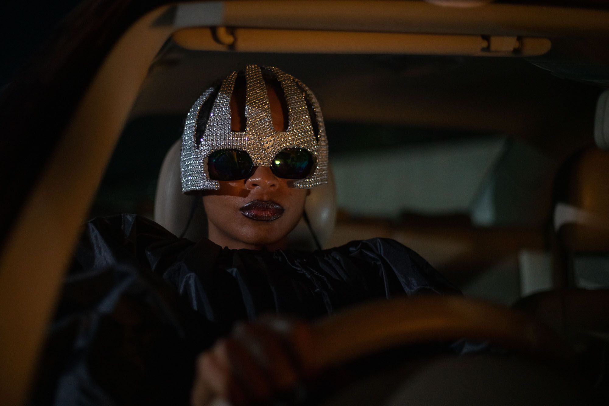 A woman drives a car wearing sunglasses and a sequined hat.