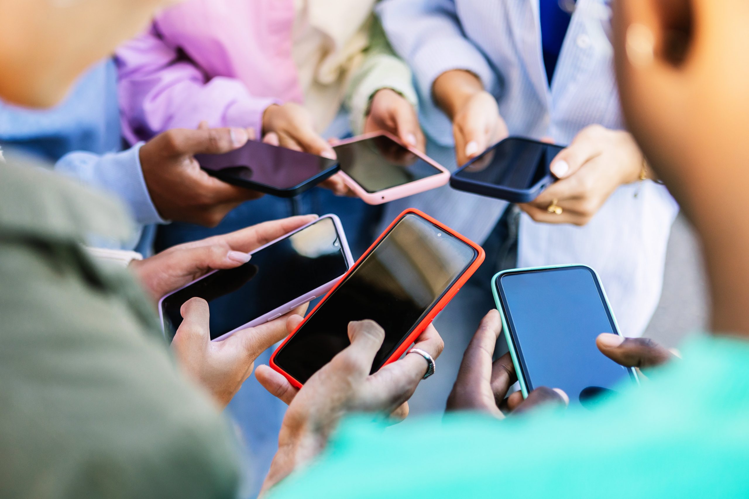 Young group of people standing in circle using mobile phones outside. Unrecognizable teen friends watching social media content on smartphone app. 