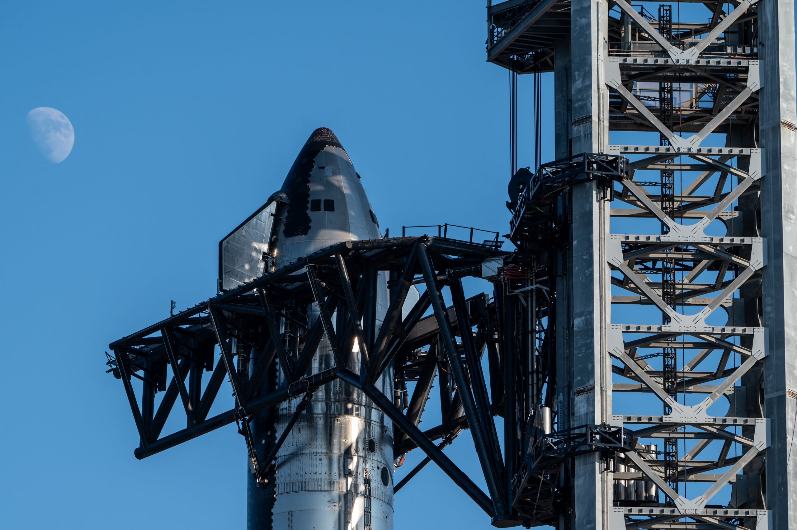 A large metal structure holds up the Space X Starship against a blue sky.