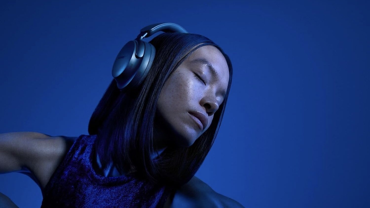 woman wearing lunar blue bose qc ultra headphones on a blue background