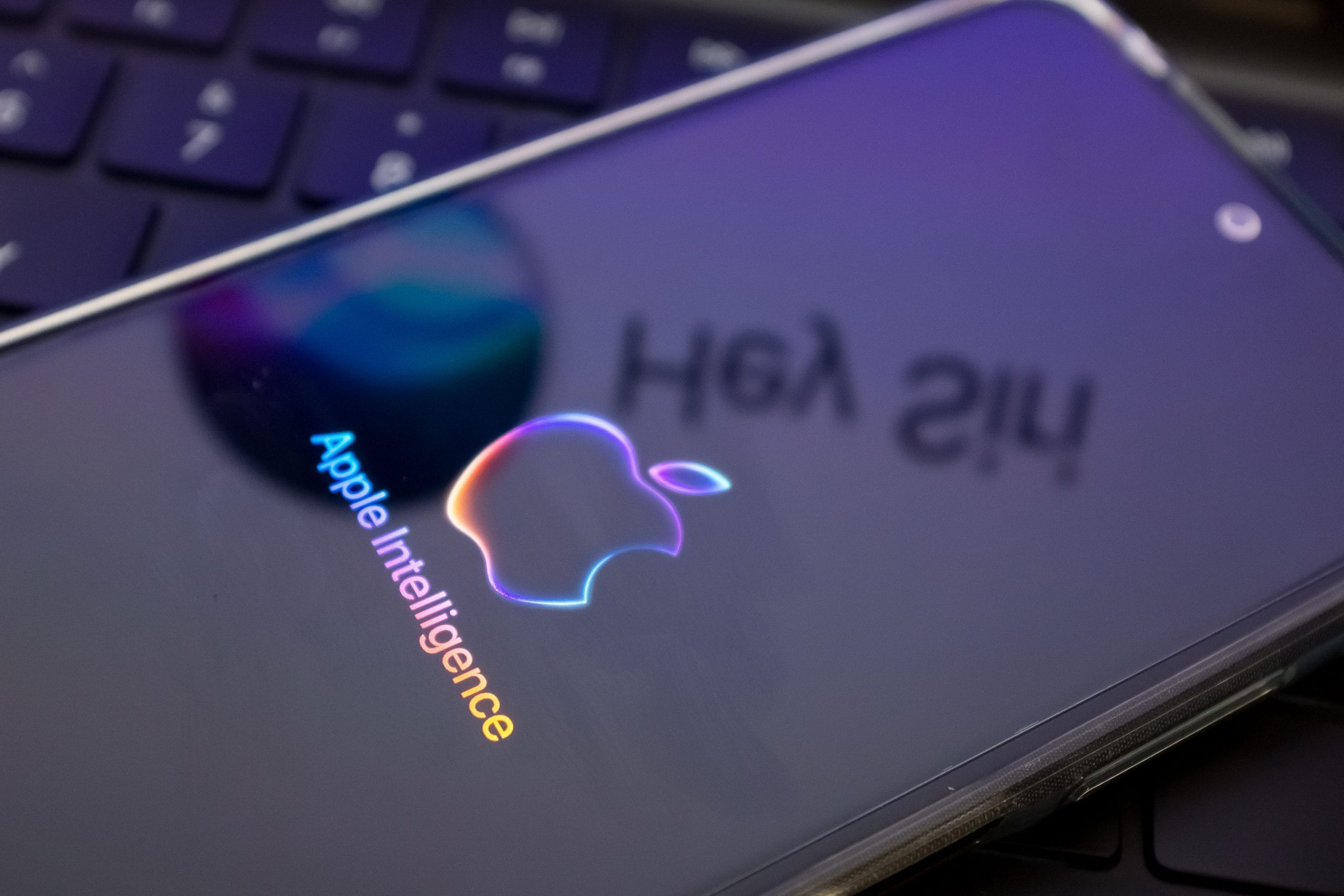 The Apple Intelligence logo is being displayed on a smartphone, with the Apple Siri logo in the background