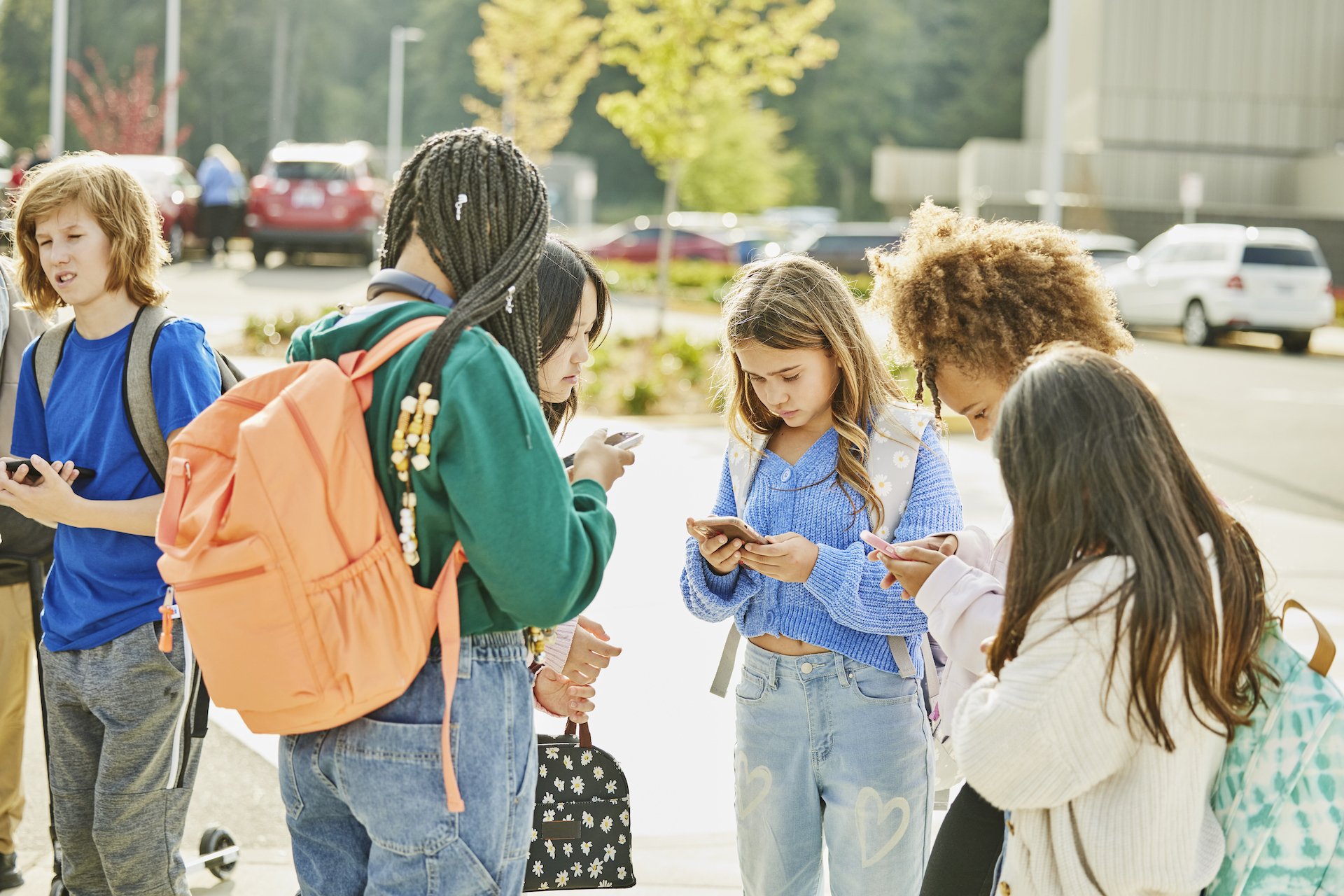 Teens gathered outside of school, all staring at their phones together.