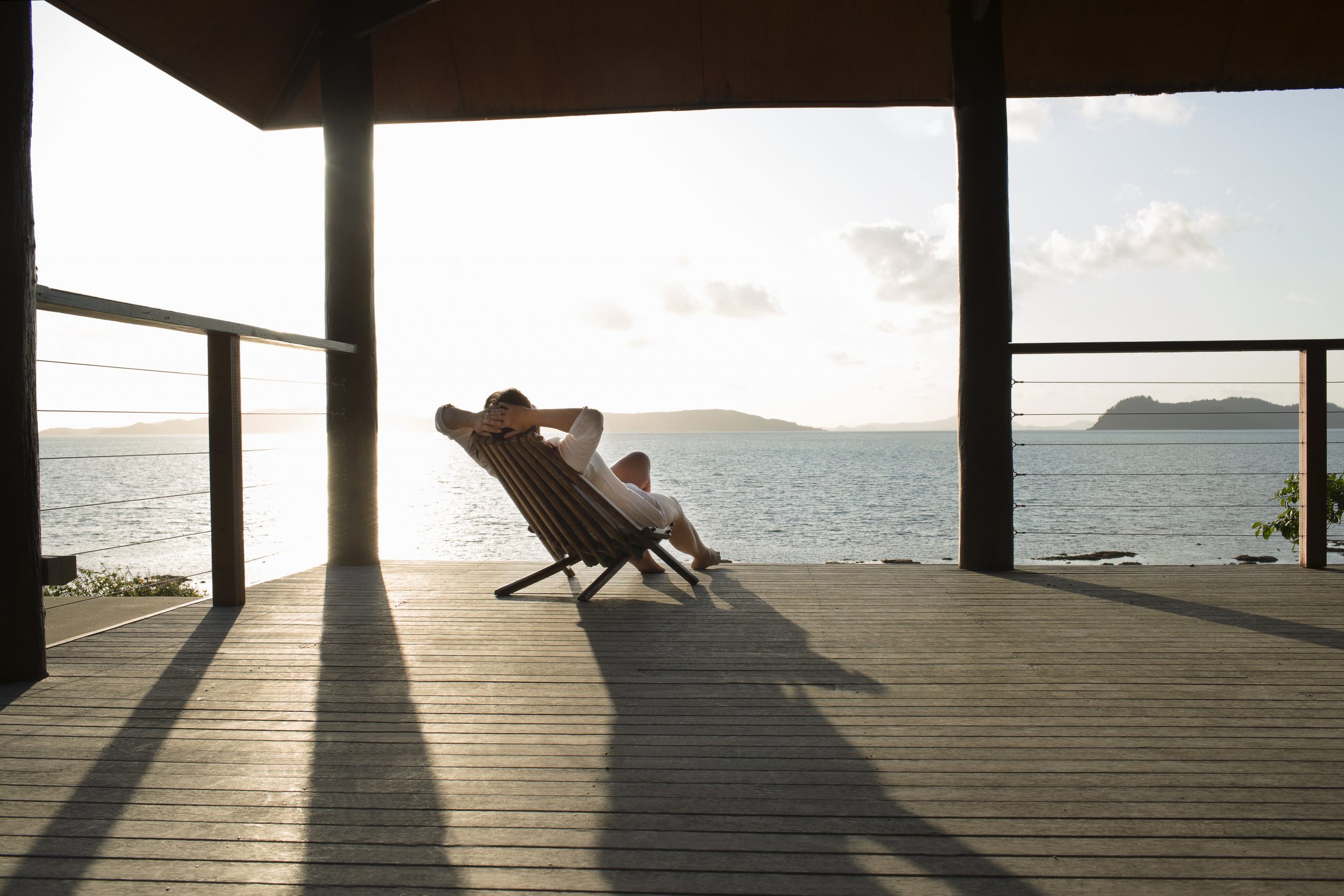 a person sits on a deck outstretched on a chair with the sun shining