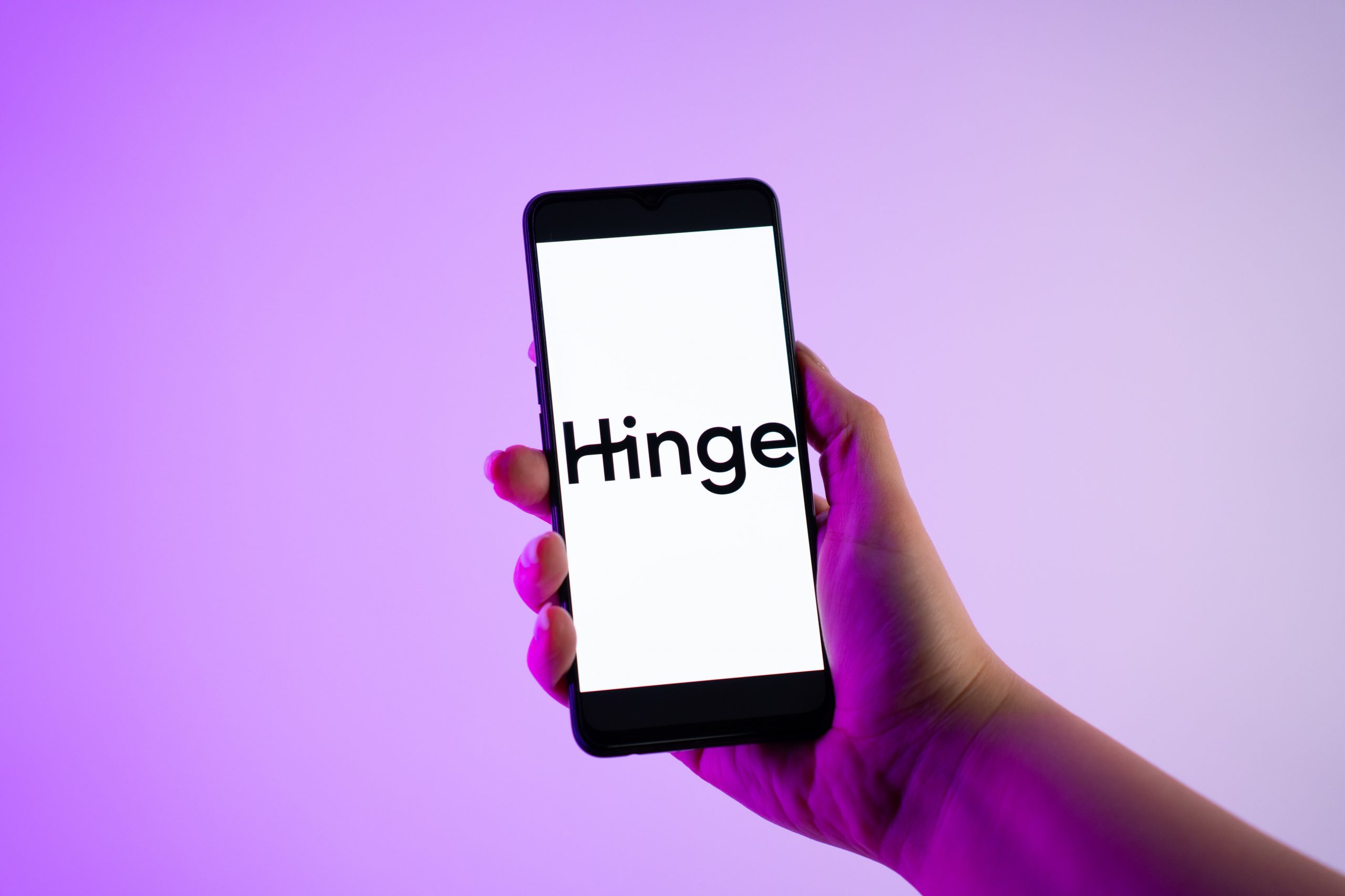 A person is holding a mobile phone with the Hinge logo on its screen